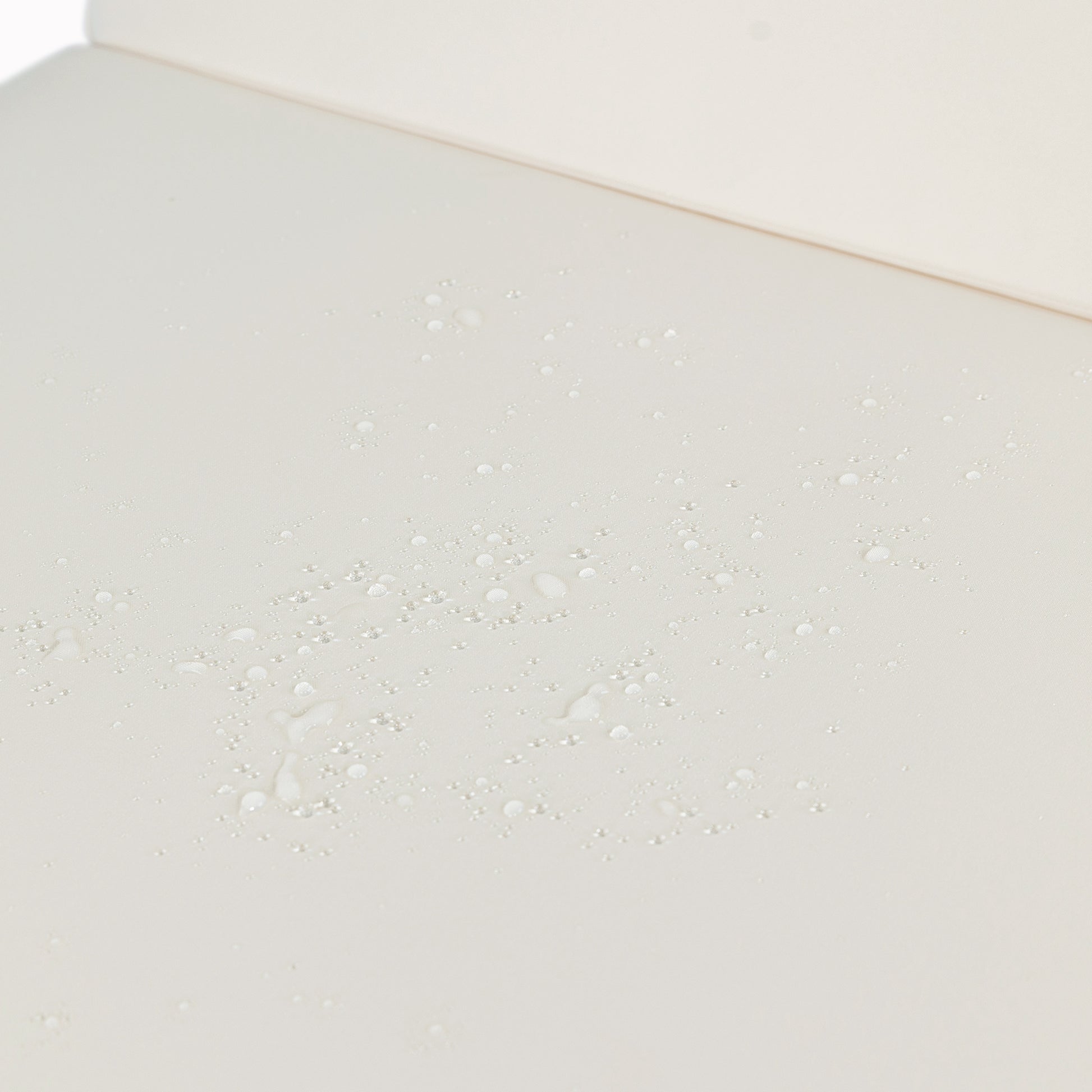 Closeup of creamcolored fabric with water droplets demonstrating its waterrepellent quality