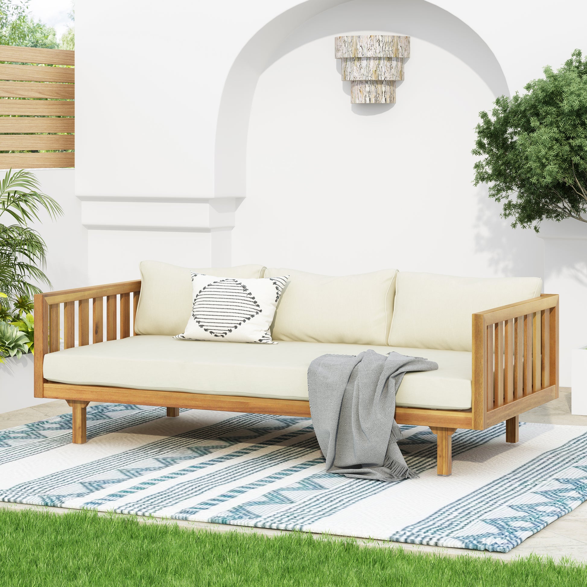 Modern acacia wood outdoor sofa with beige cushions and gray throw blanket