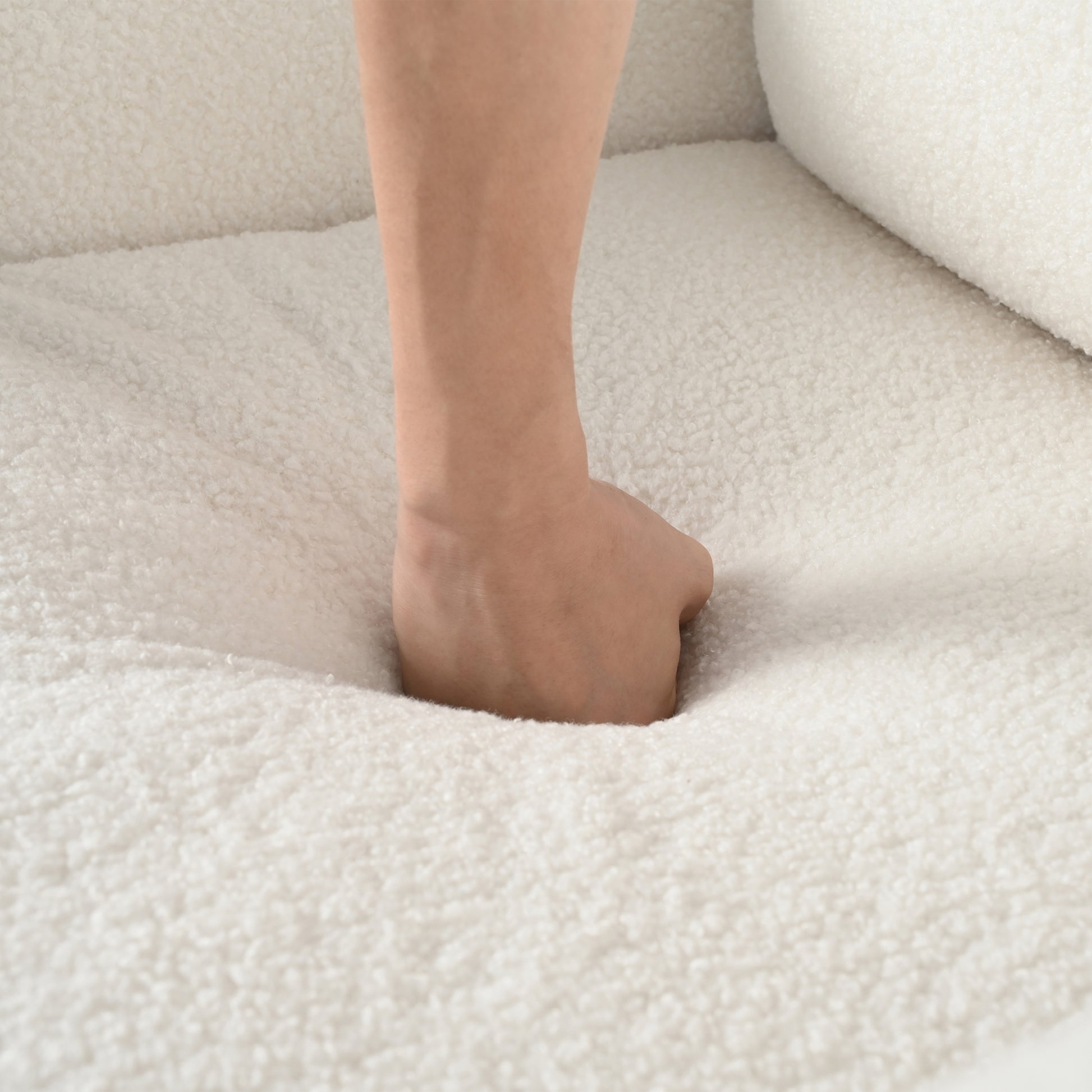 Hand pressing into plush ivory teddy bear fabric for sofa showing softness