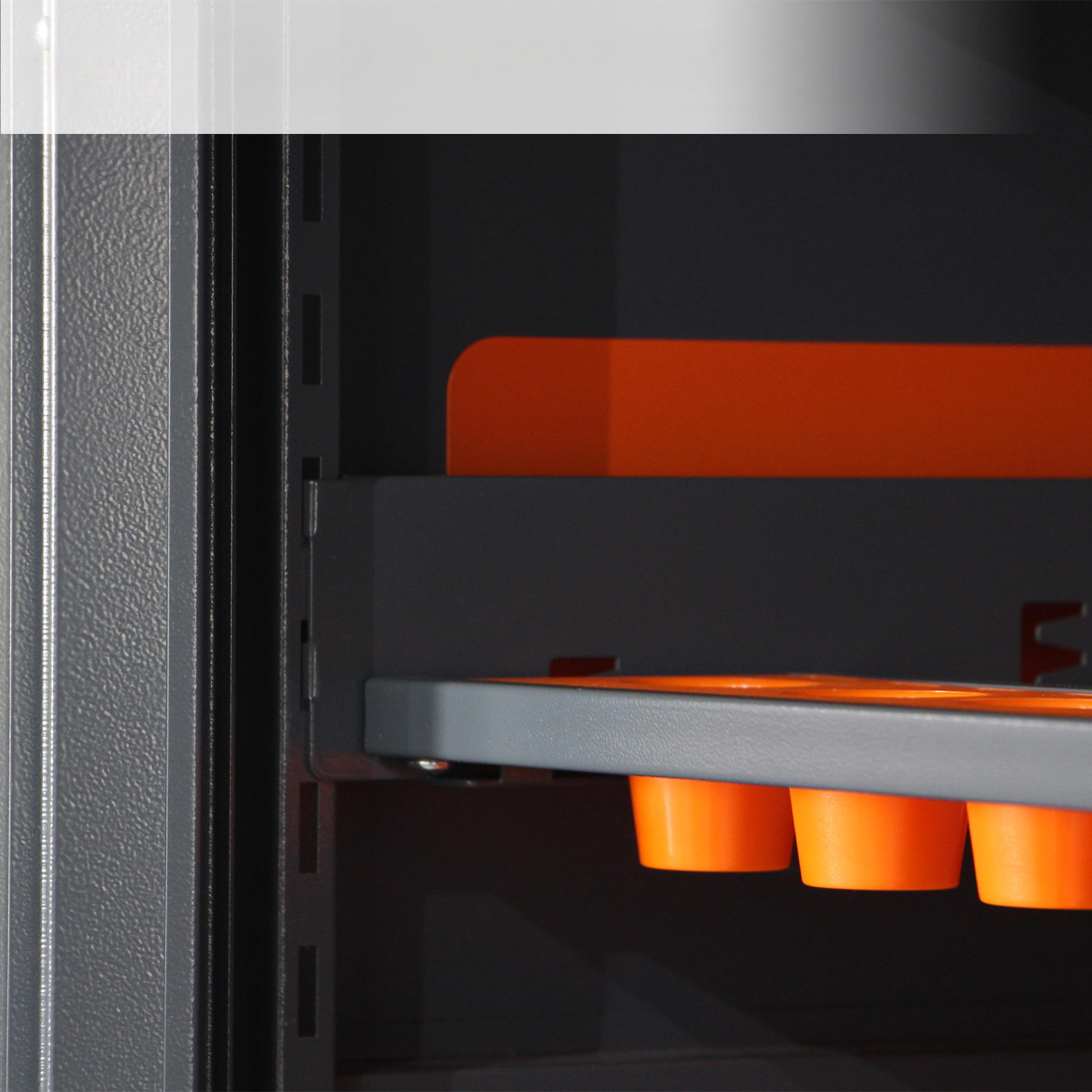Dark grey metal cabinet interior with bright orange cup holders on a shelf