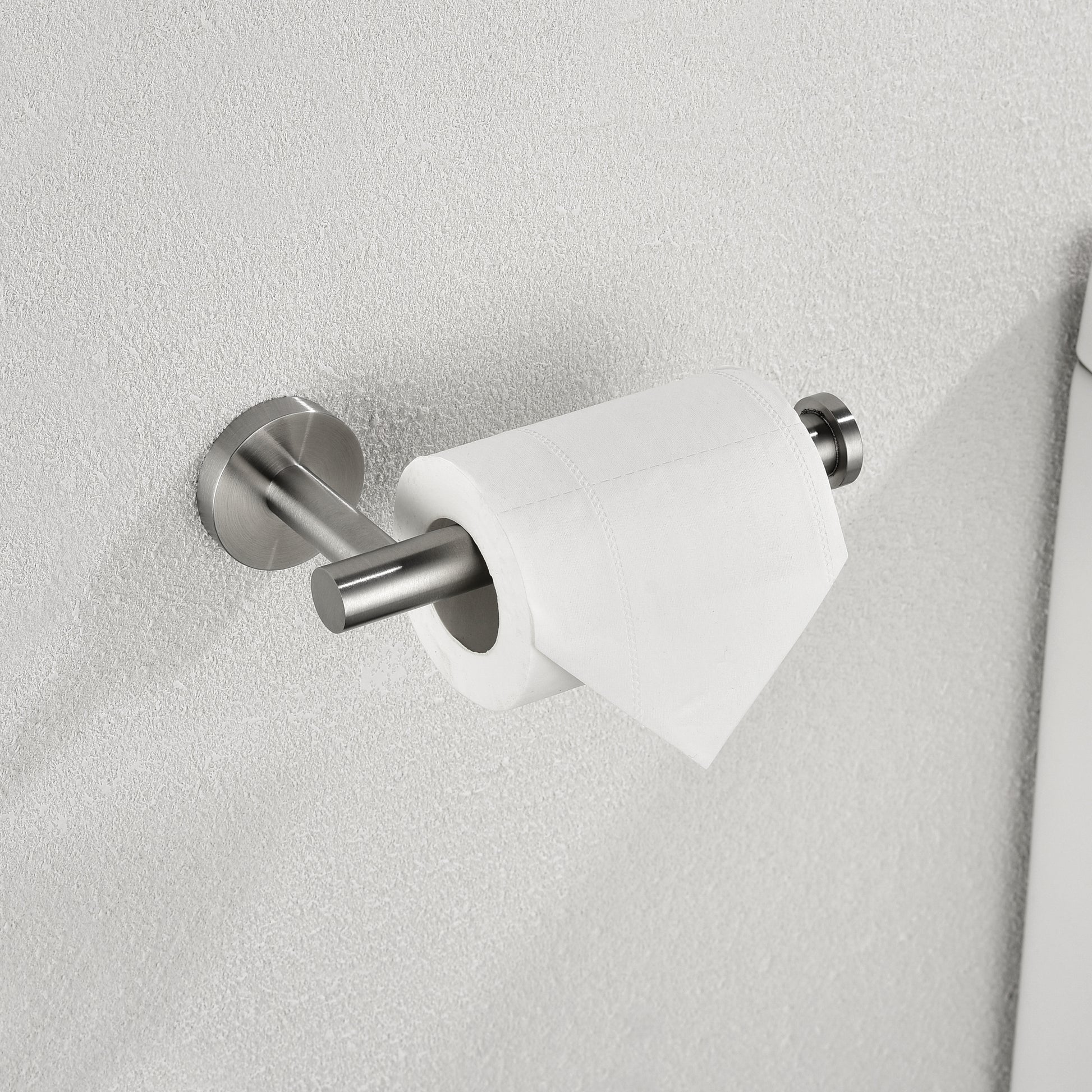 Brushed nickel toilet paper holder mounted on a textured gray wall with a white toilet paper roll