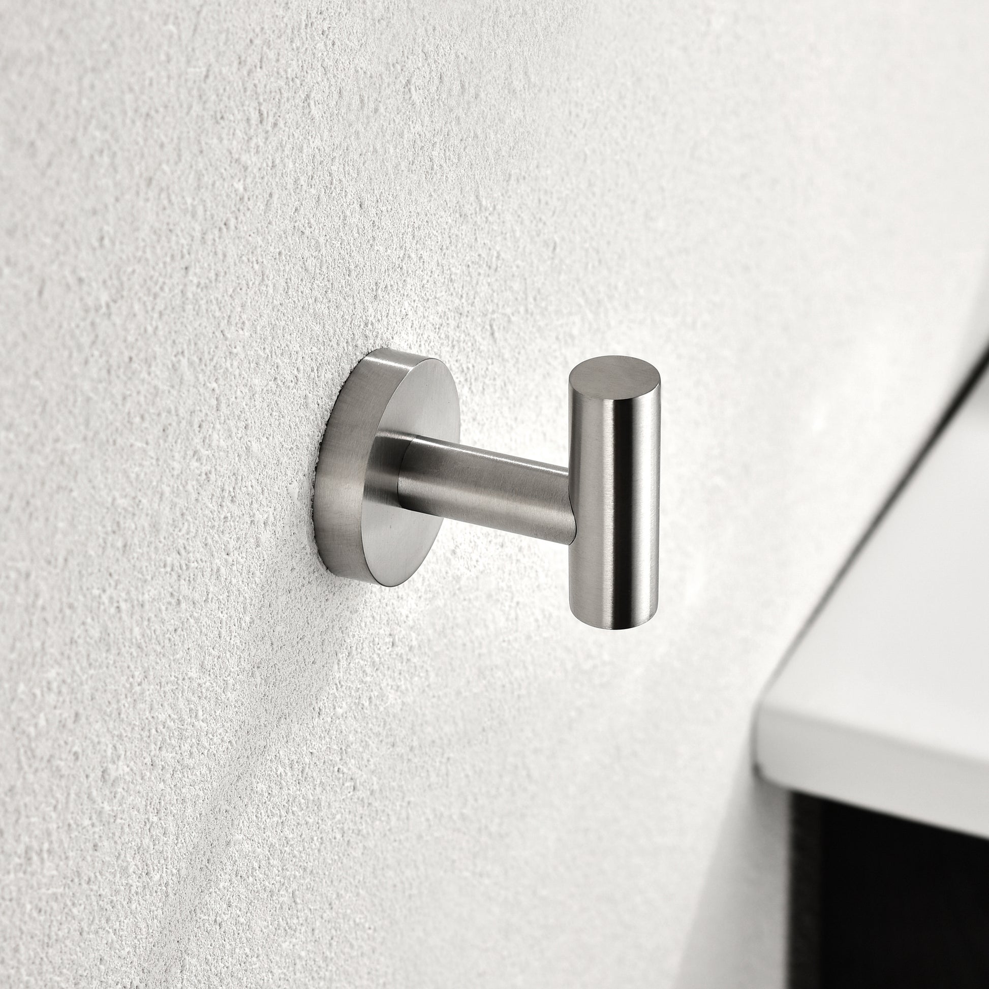 Brushed nickel towel hook with minimalist design on textured white wall