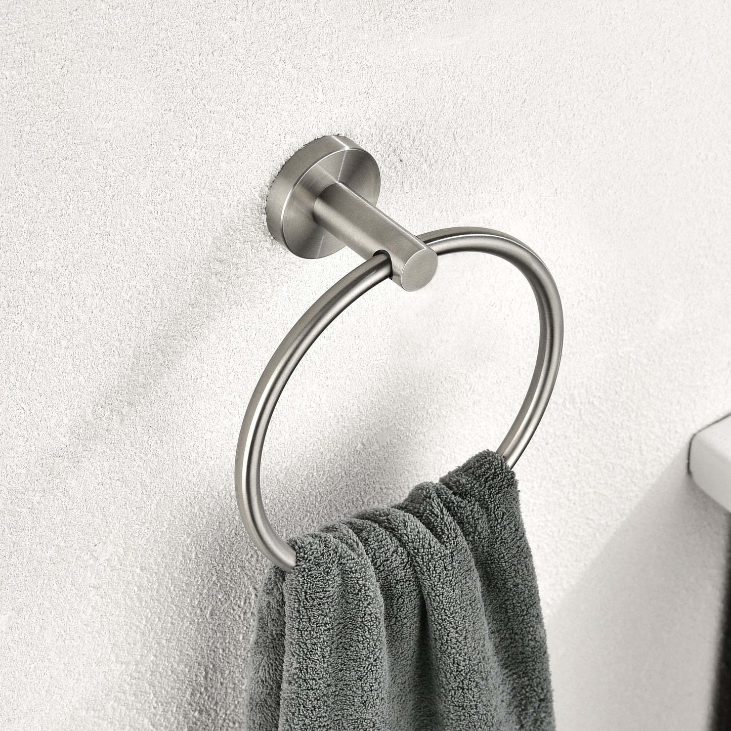 Brushed nickel towel ring mounted on textured wall with a grey hand towel