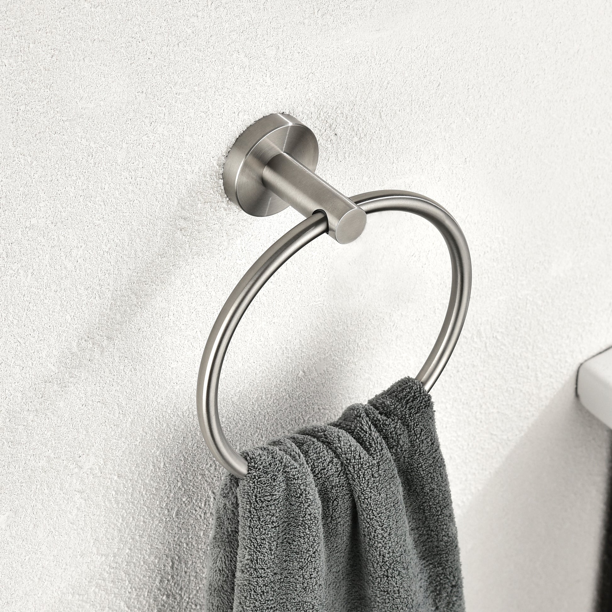 Brushed nickel towel ring mounted on textured wall with a grey hand towel