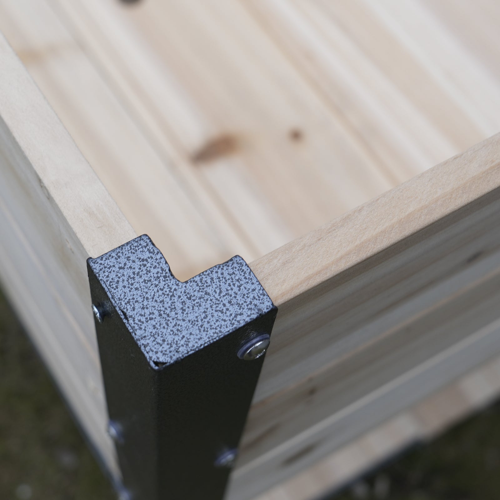 Detail of a wooden raised garden bed corner with dark grey metal bracket and screws