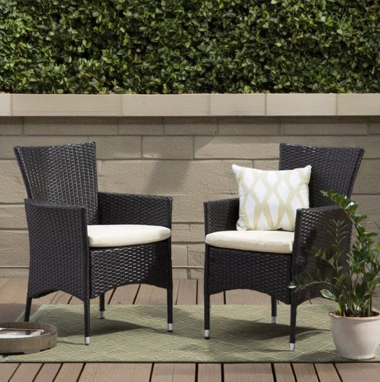 Two dark brown rattan patio chairs with cream cushions one with a diamondpatterned pillow