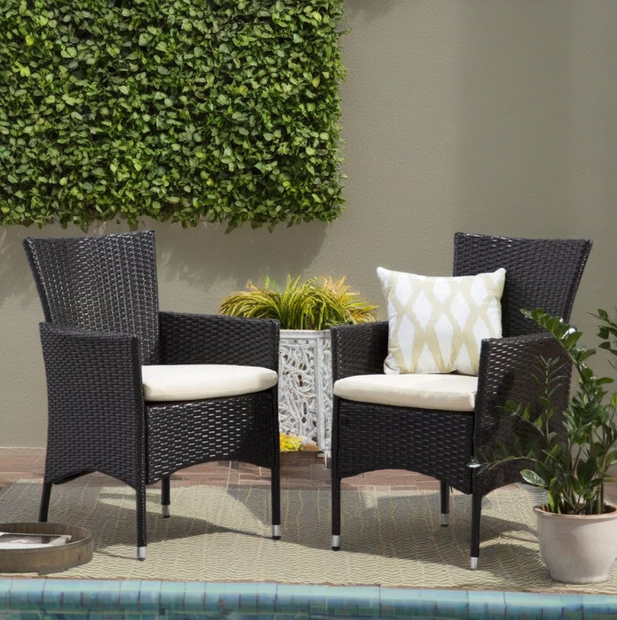 Two black wicker patio chairs with cream cushions on a rug by a pool