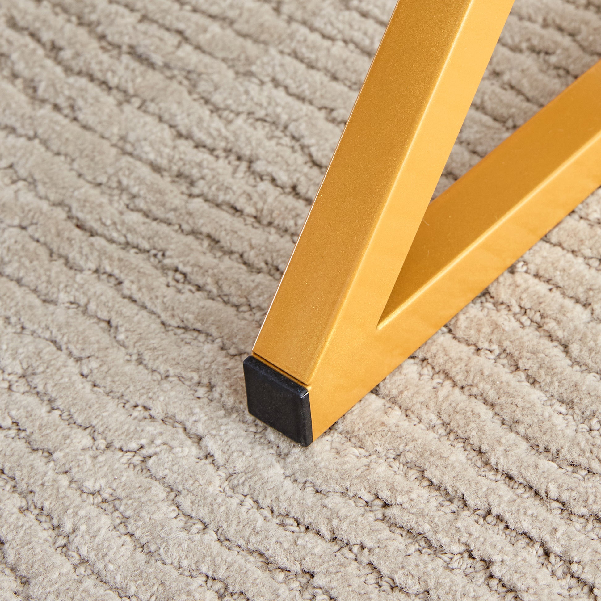 Gold metal table leg with black foot on a textured beige carpet