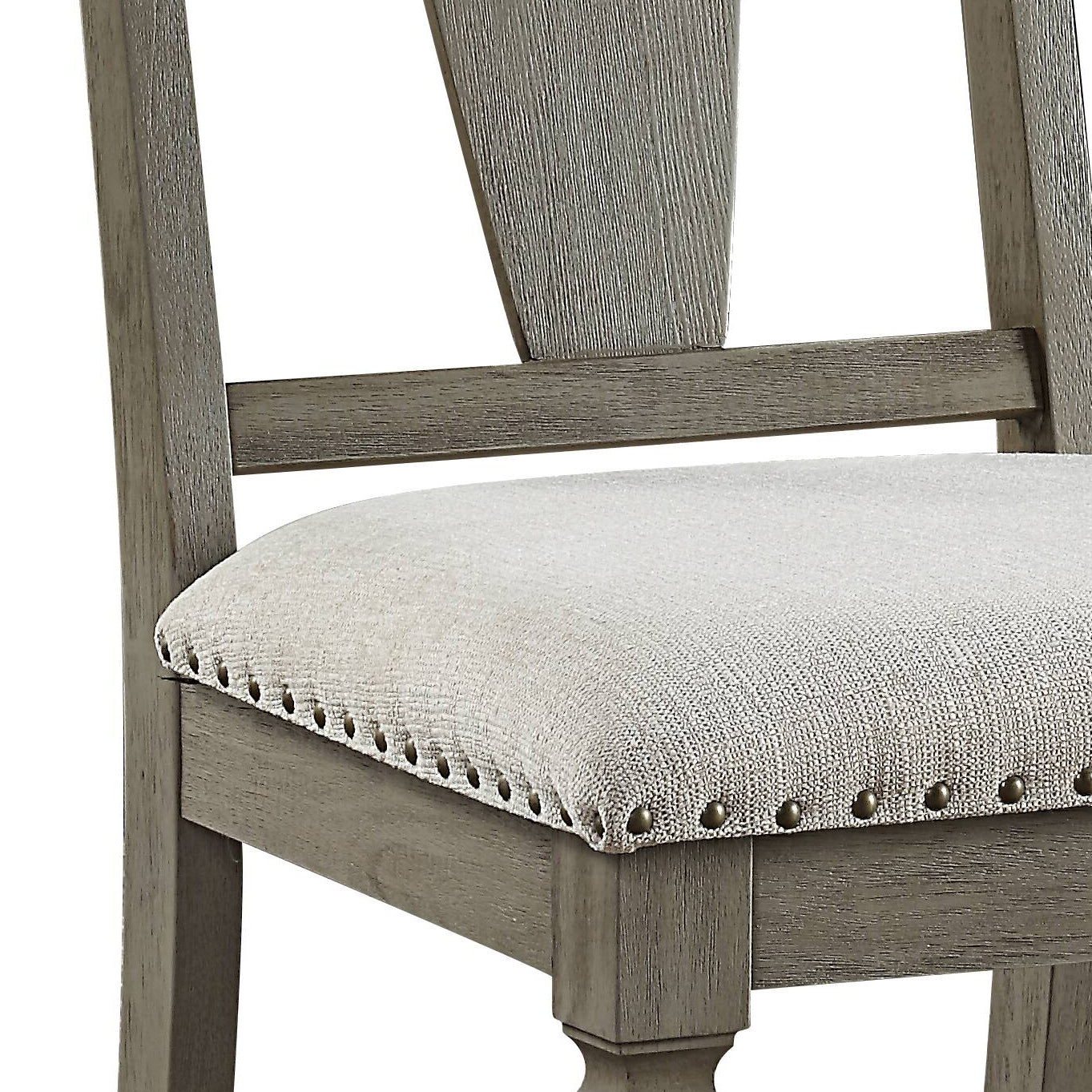 Detail of a rustic gray wooden dining chair with a light beige upholstered seat and brass tack trim
