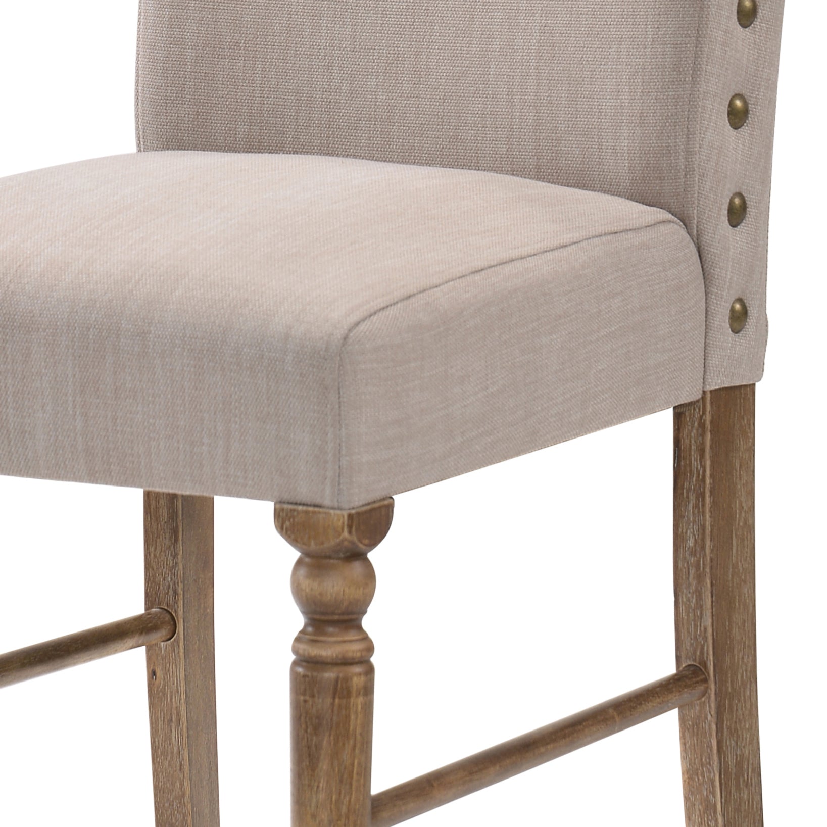 Closeup of a beige upholstered bar stool with brass nailhead trim and wooden legs