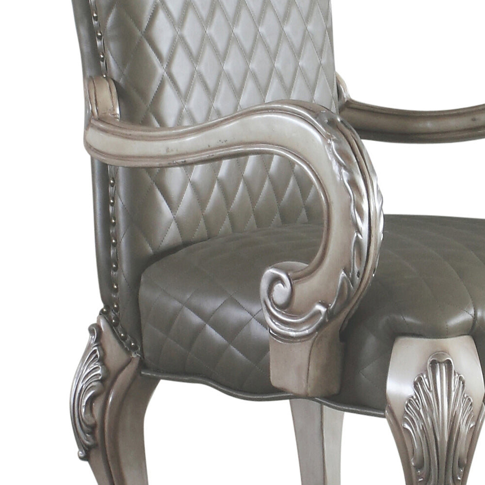 Closeup of an antique armchair armrest with tufted taupe upholstery and ornate carved wood detailing