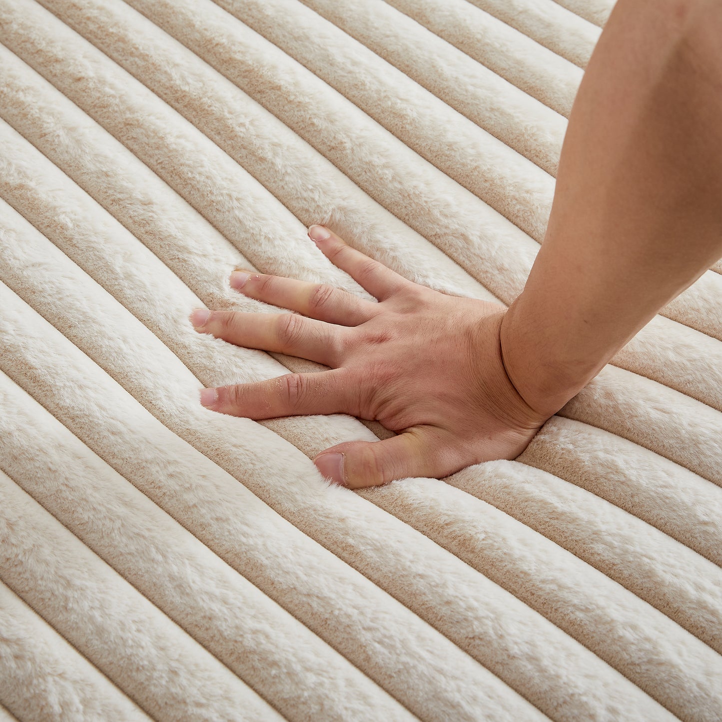 Closeup of a hand pressing into plush creamcolored faux fur blanket with ribbed texture