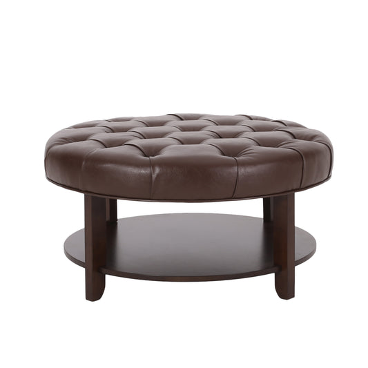 Tufted brown faux leather round ottoman with dark wood legs and lower shelf