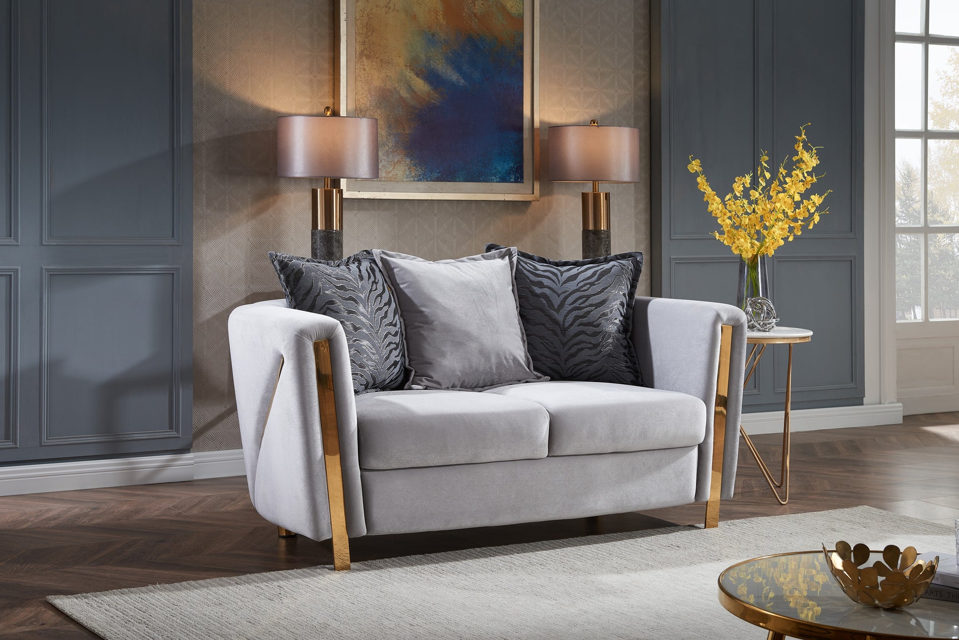 Plush grey velvet loveseat with gold metal accents and decorative throw pillows