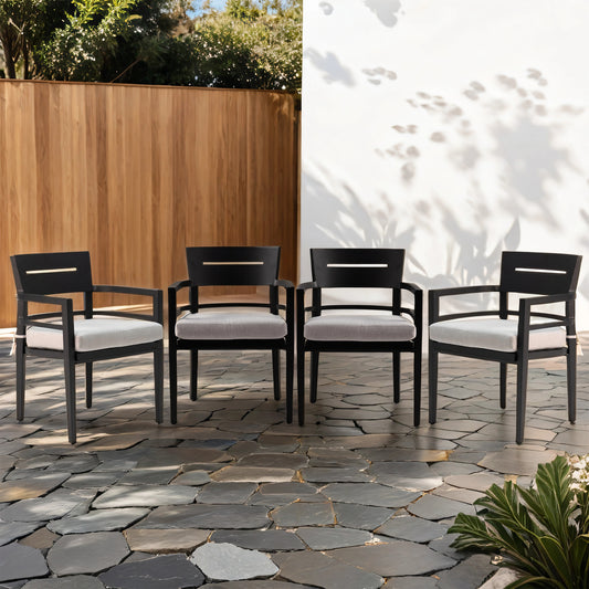 Four modern black metal patio chairs with light grey cushions arranged on flagstone
