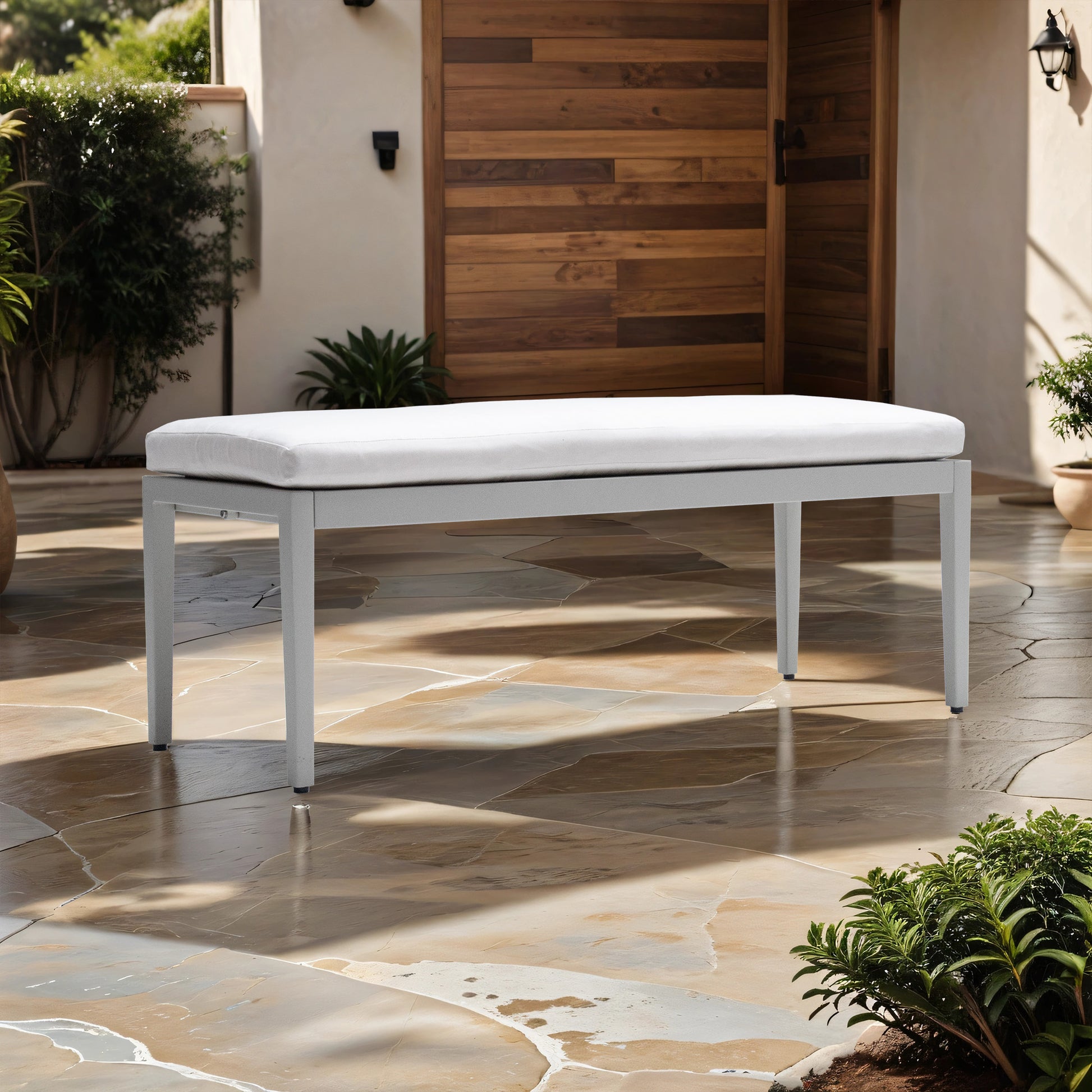 Modern grey metal bench with plush white outdoor cushion on flagstone patio