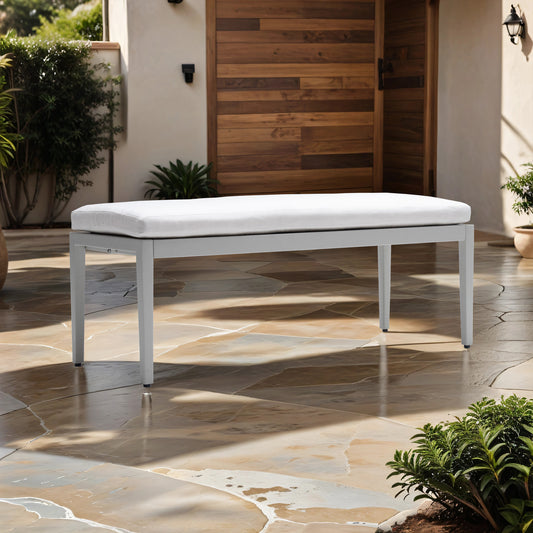 Modern grey metal bench with plush white outdoor cushion on flagstone patio