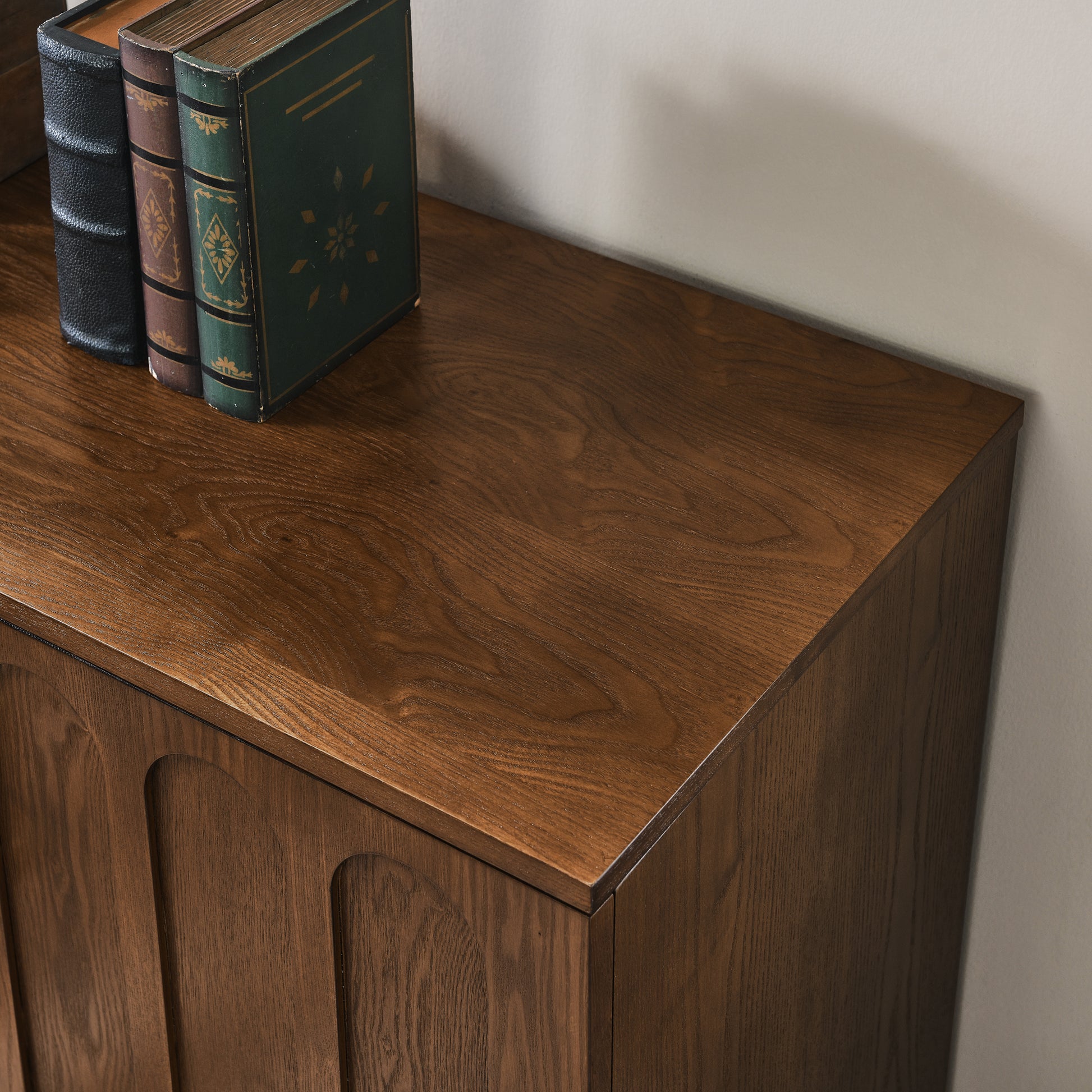 Dark brown wooden sideboard with embossed arched doors and ornate books on top