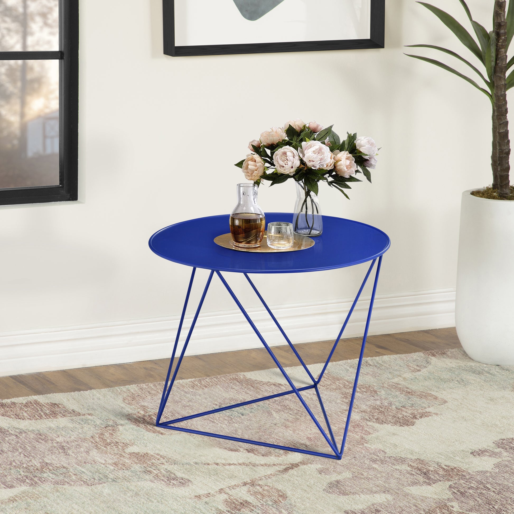 Vibrant blue metal round accent table with geometric legs holding decorative vase and carafe