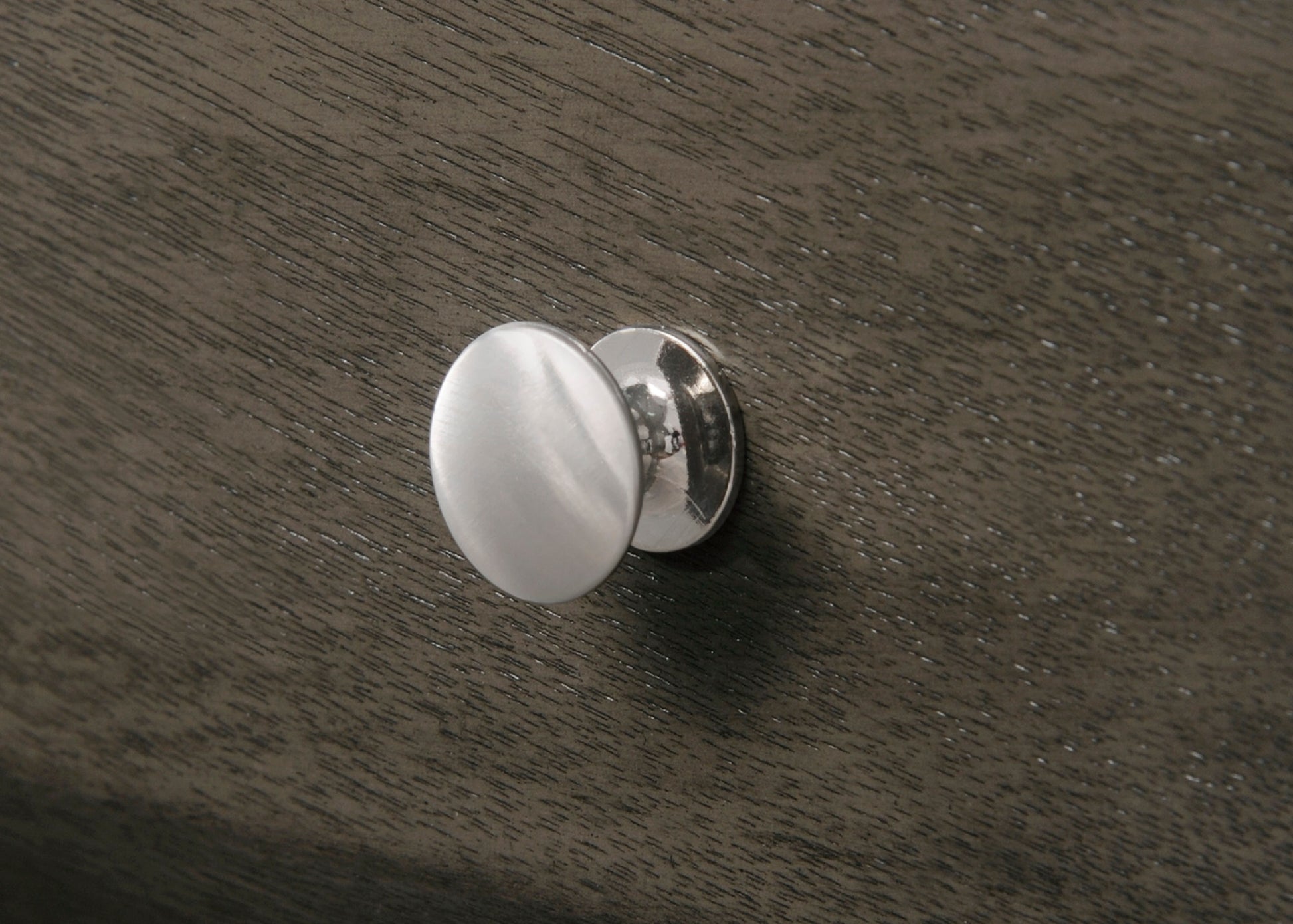 Brushed nickel oval cabinet knob on textured dark wood grain drawer front
