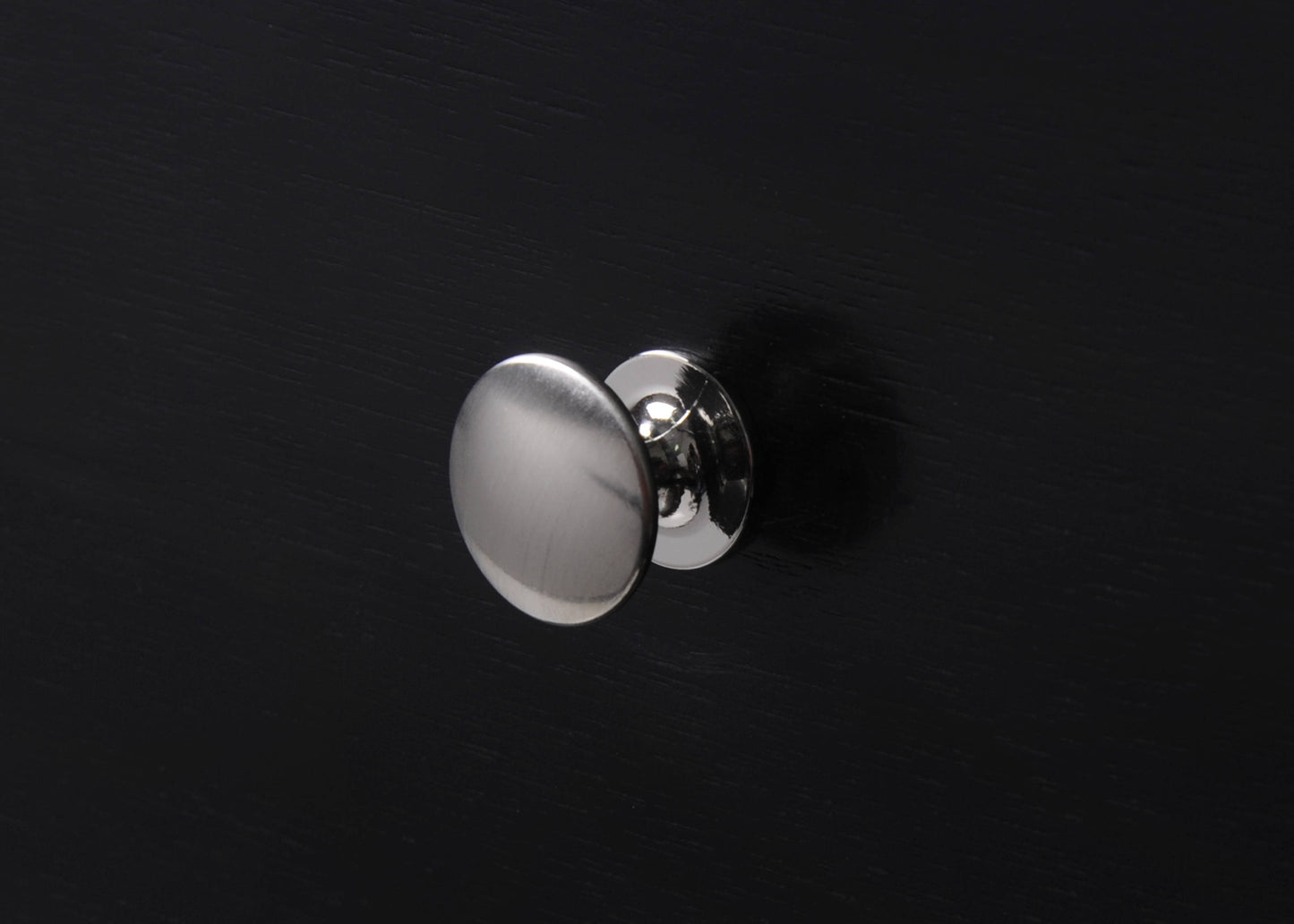 Brushed nickel round cabinet knob on a black wooden surface