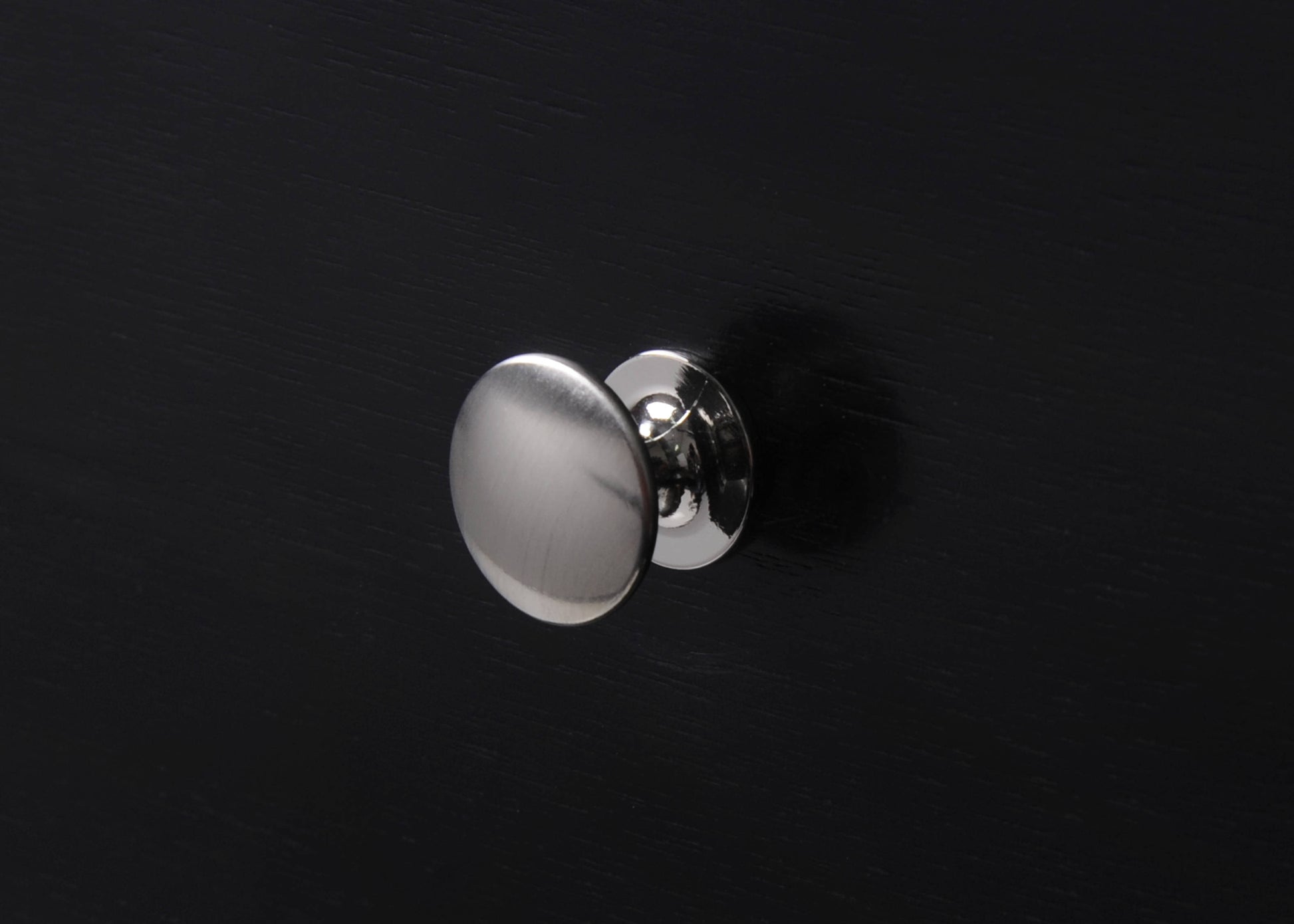 Brushed nickel round cabinet knob on a black wooden surface
