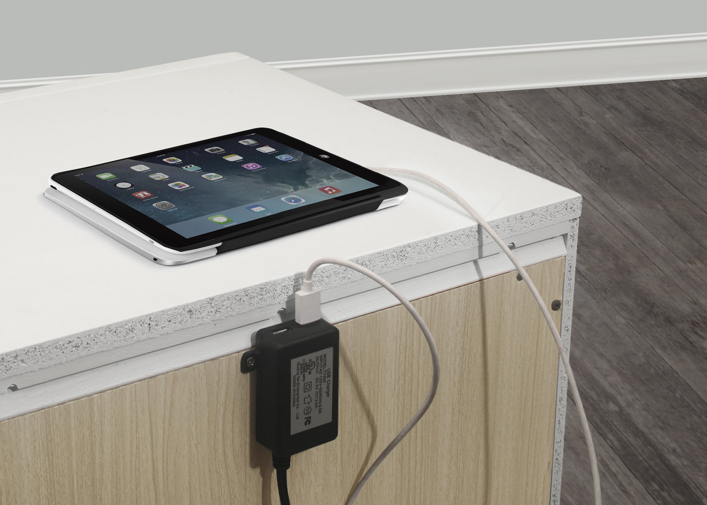 Silver tablet charging on a white surface with a USB adapter plugged into the side
