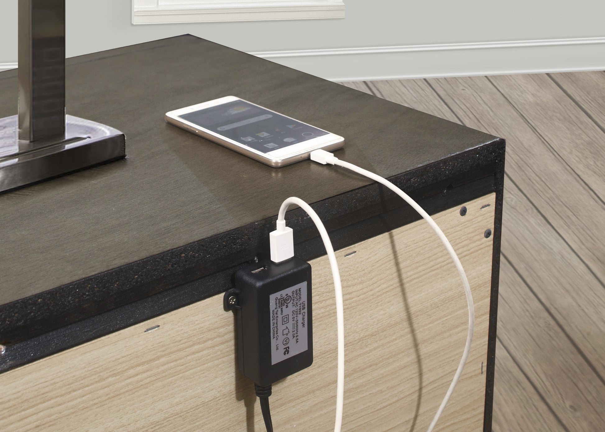 White smartphone charging via USB power adapter attached to a dark wood table