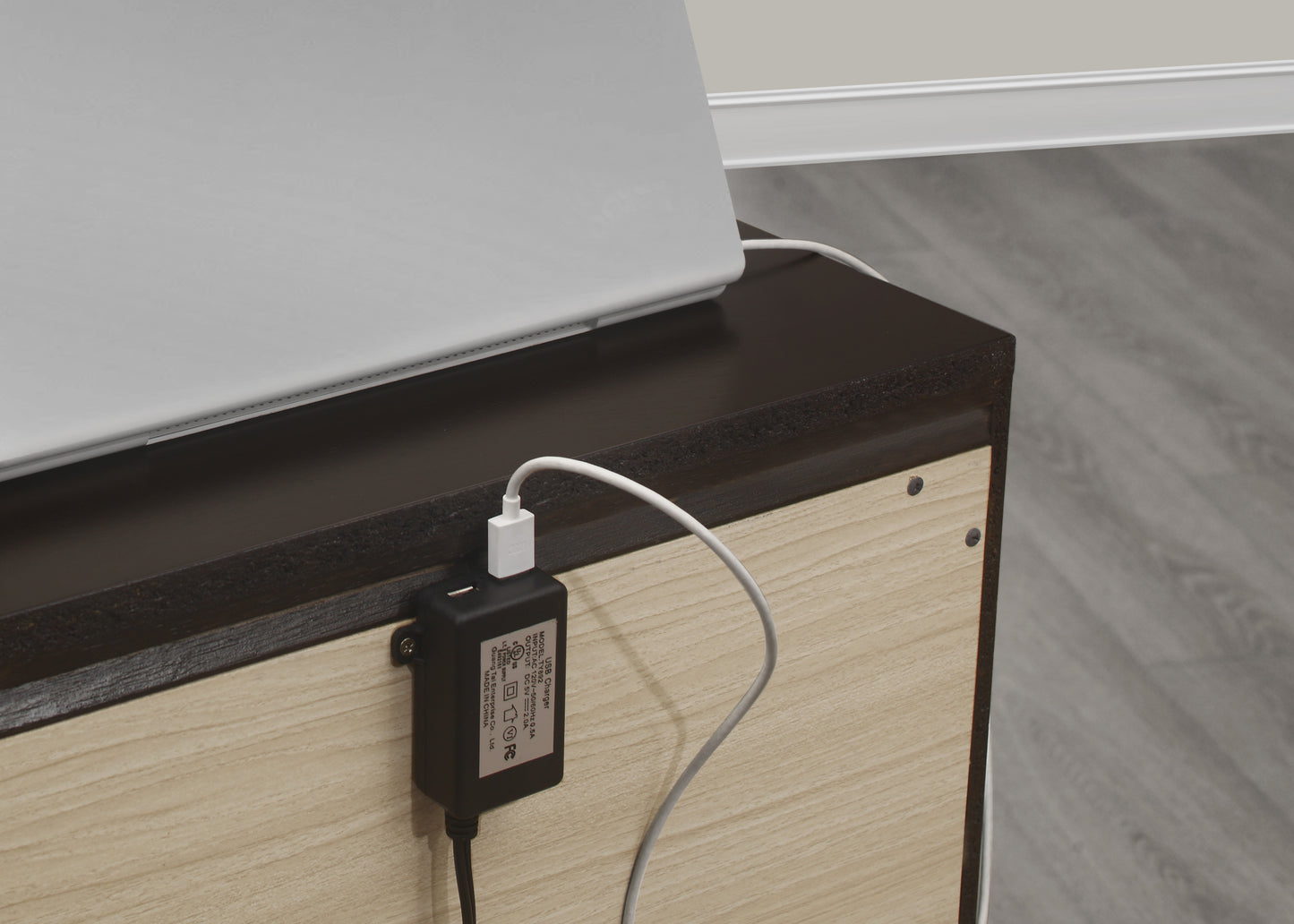 Black USB charger adapter plugged into a white laptop charging cable on a wooden surface
