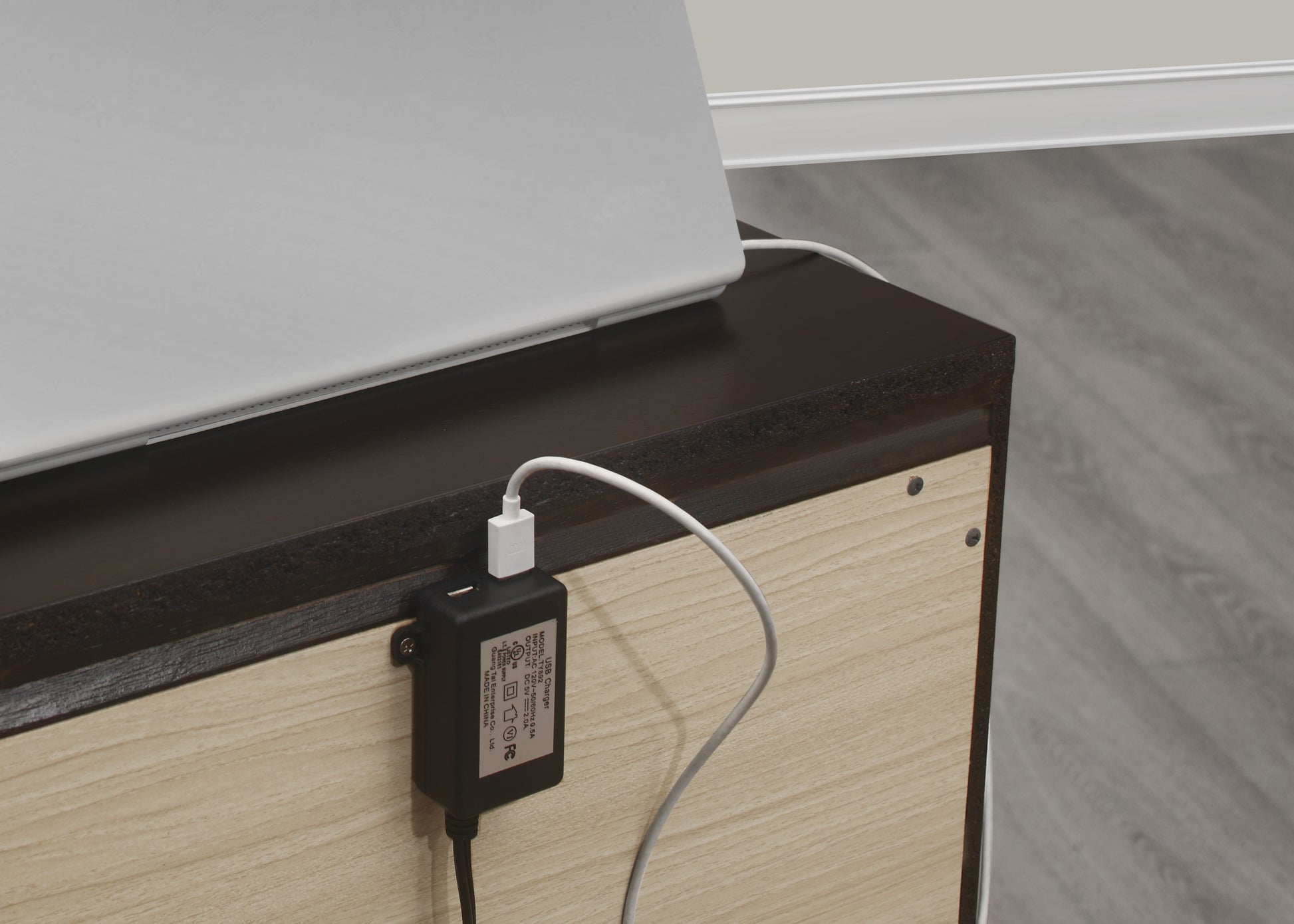 Black USB charger adapter plugged into a white laptop charging cable on a wooden surface
