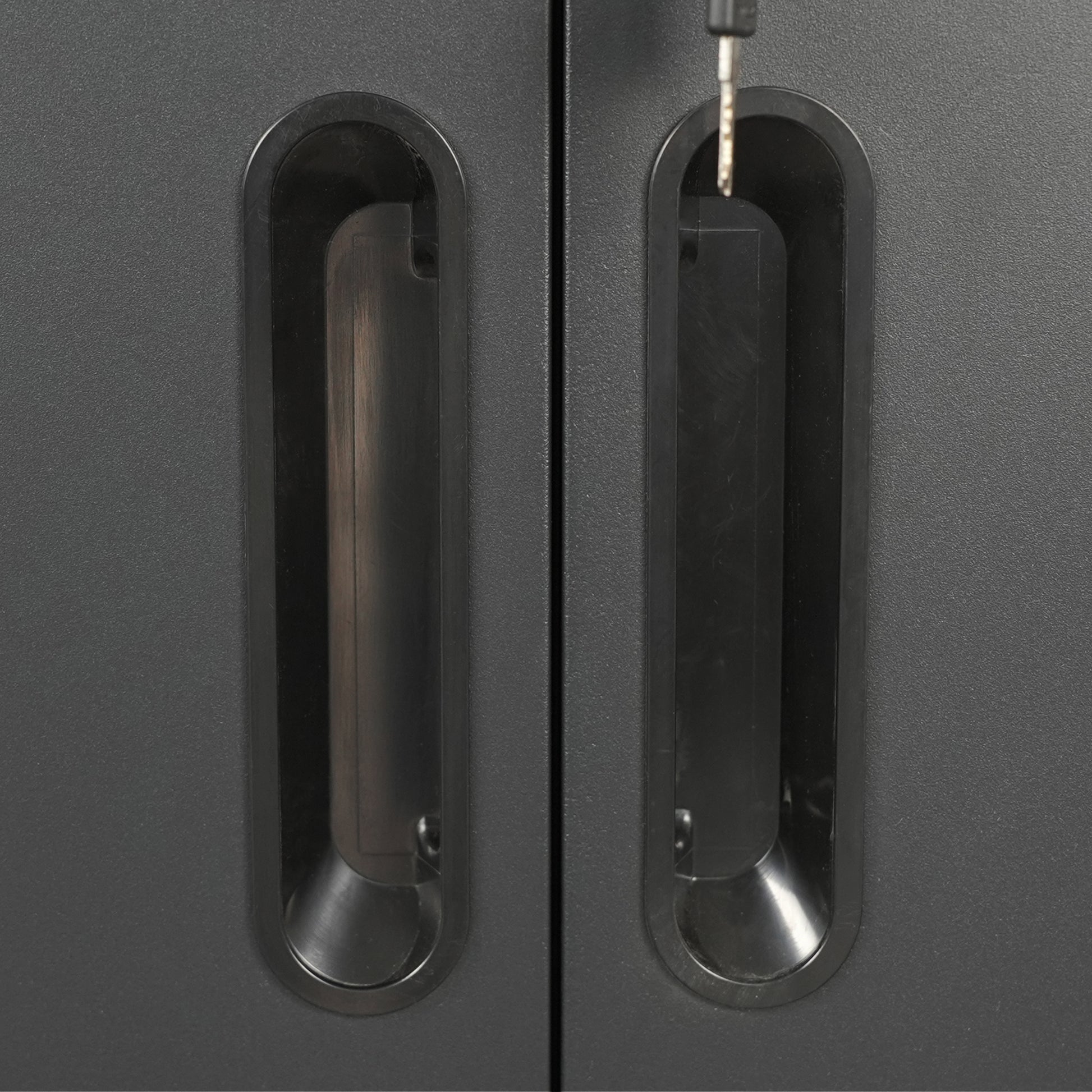 Closeup of two dark grey metal filing cabinet doors with integrated black handles and one key inserted