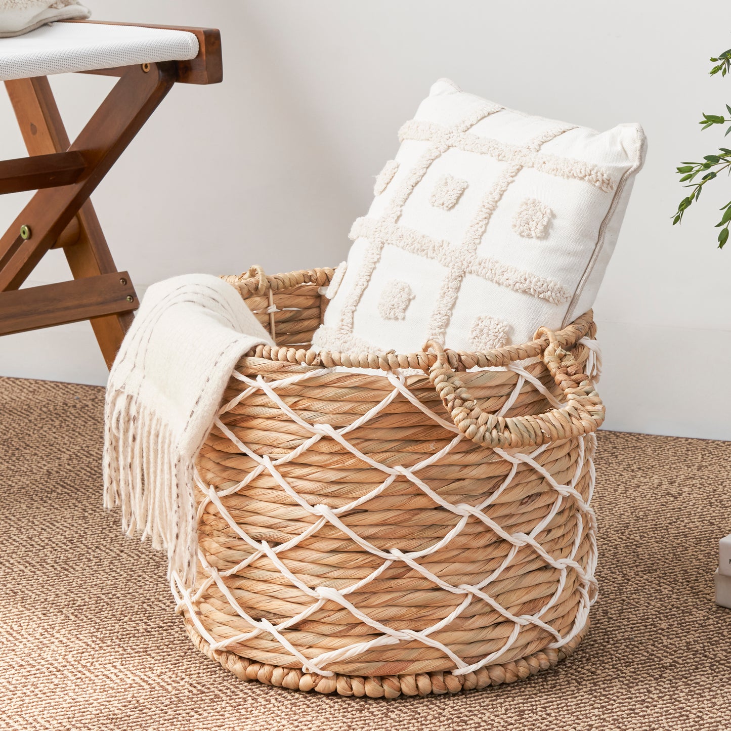 Woven hyacinth basket with white rope accents holding a textured cream pillow and throw