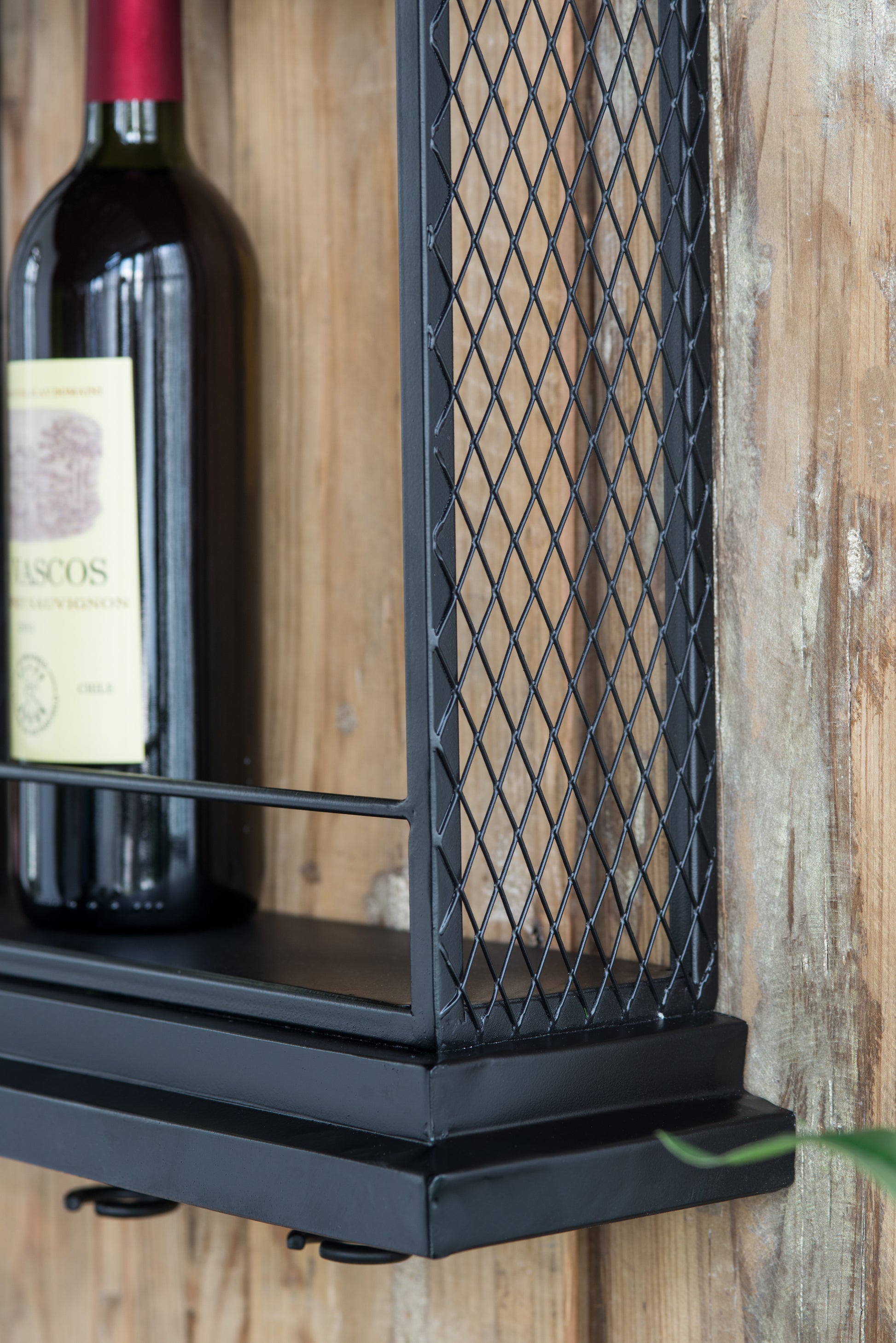 Industrial black metal wall shelf with diamond grid detail holding a red wine bottle