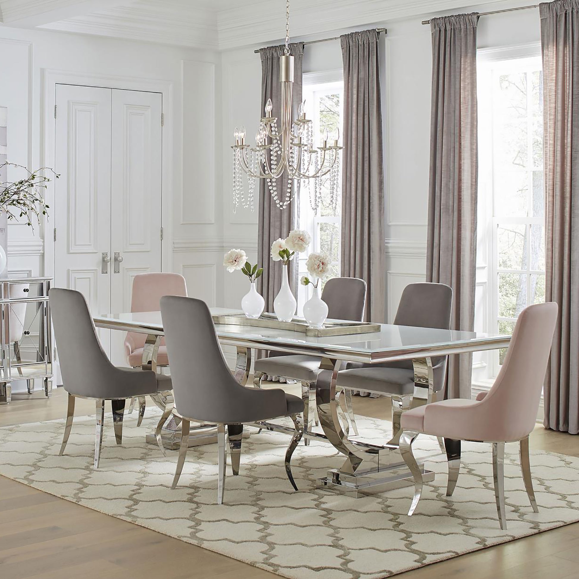 Modern glass dining table with chrome base and upholstered chairs in grey and blush pink