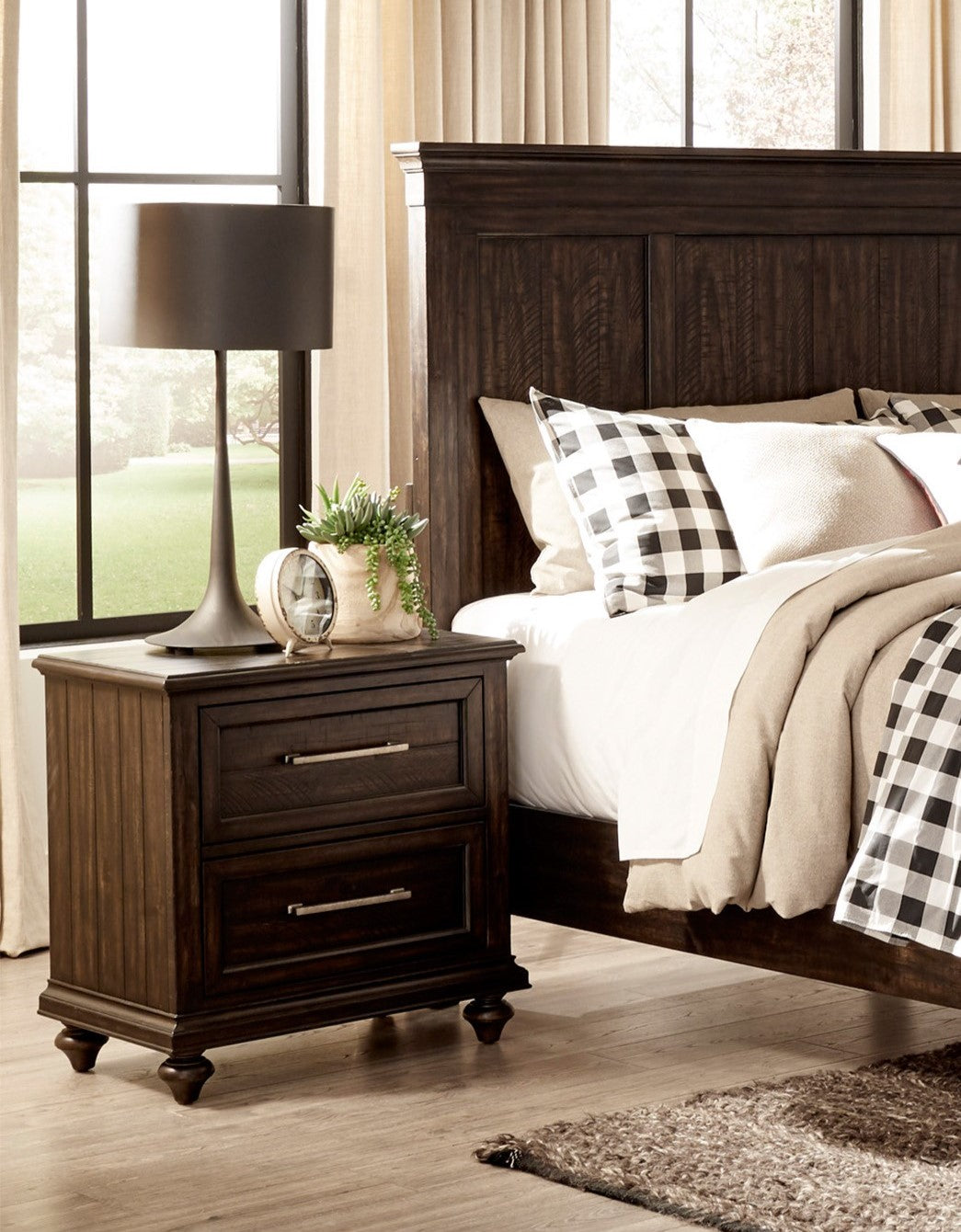 Dark wood nightstand with two drawers and decorative carved legs next to a bed