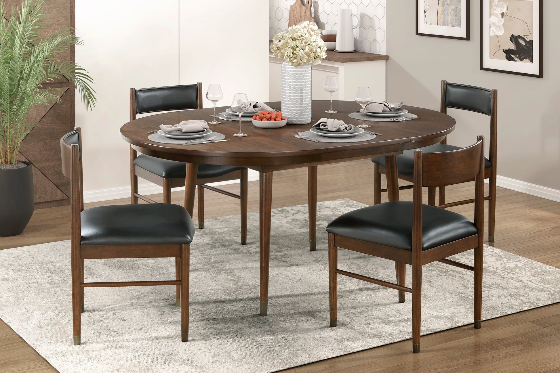 Dark wood oval dining table with four black leather chairs and place settings