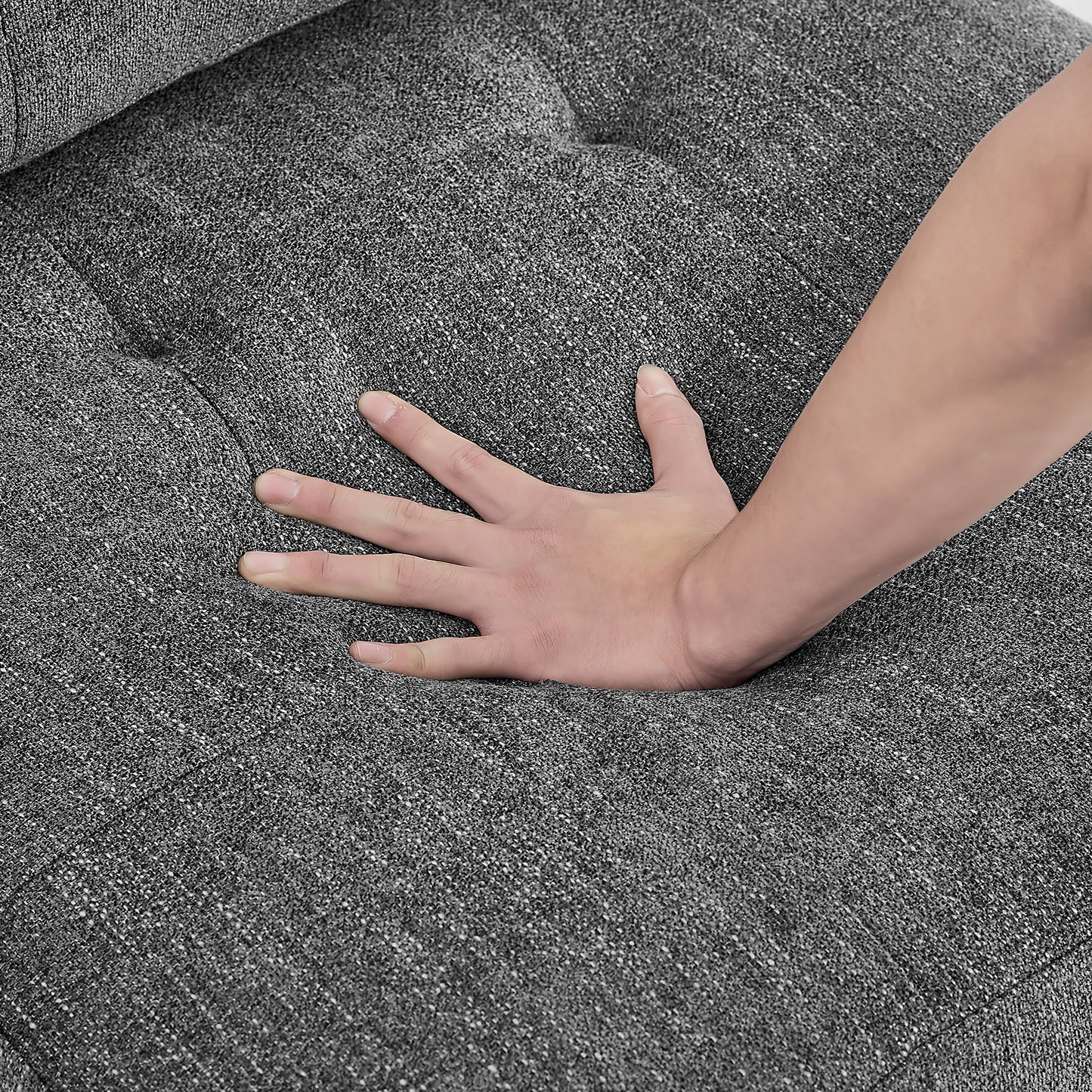 Closeup of a hand pressing into a plush grey fabric sofa cushion showcasing its softness and texture