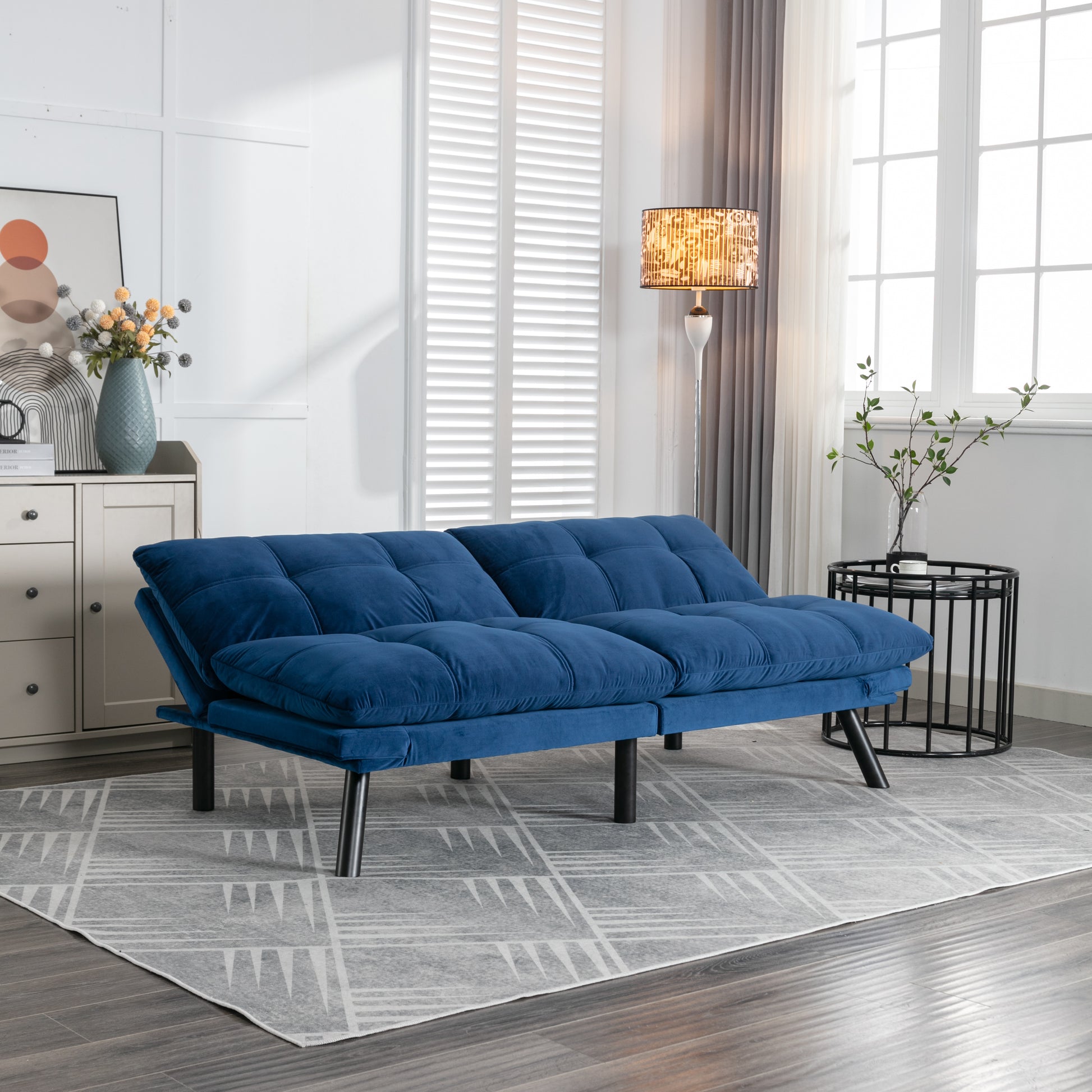 Plush navy blue velvet sofa bed with tufted cushions and sleek black legs in a modern living room