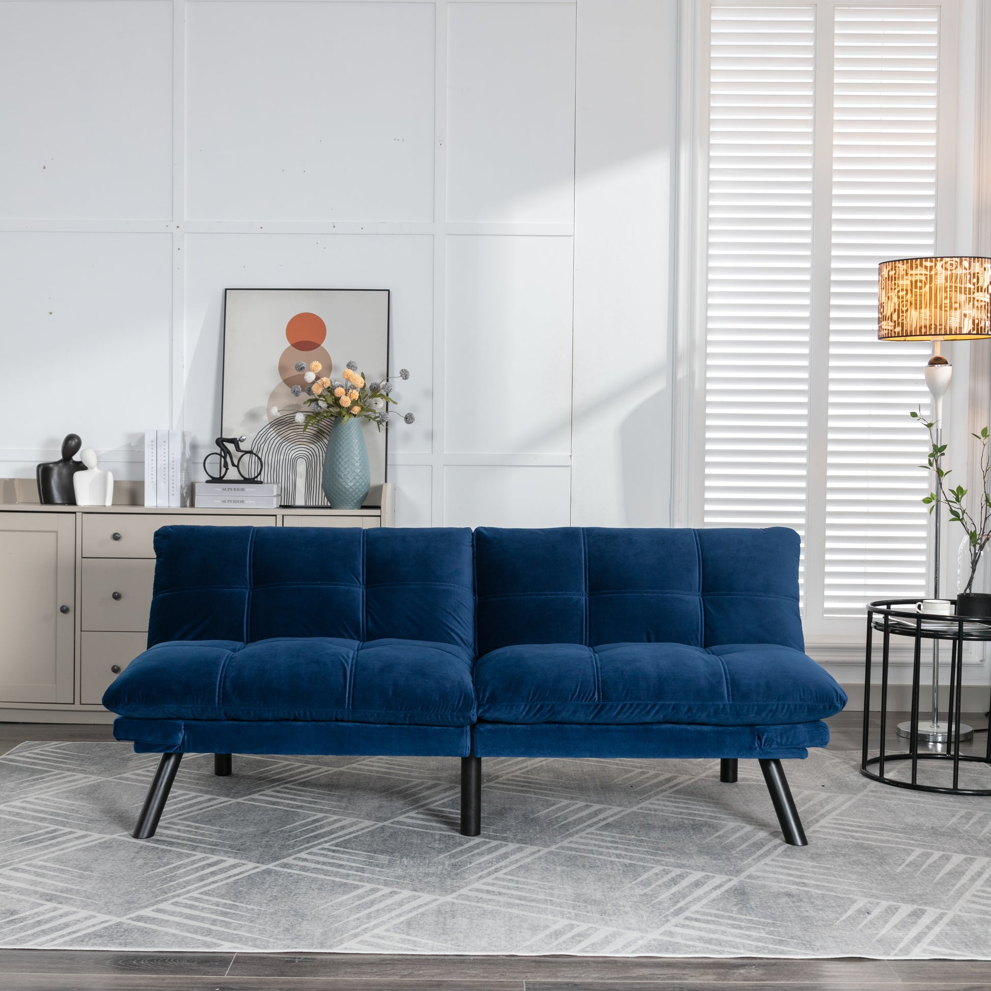 Plush velvet futon in deep navy blue featuring button tufting and sleek black legs perfect for small spaces