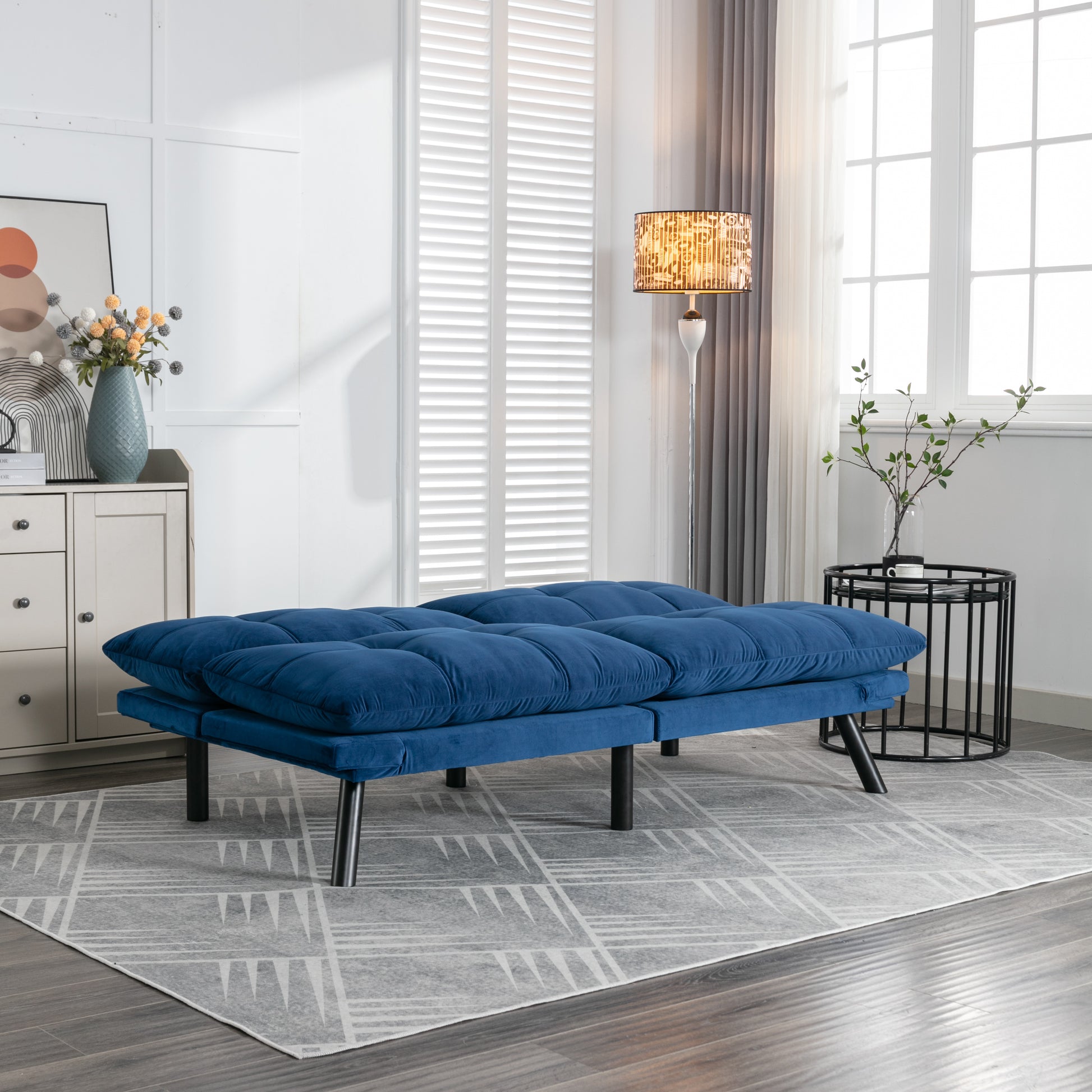 Tufted navy blue velvet futon sofa with black metal legs on a geometric rug