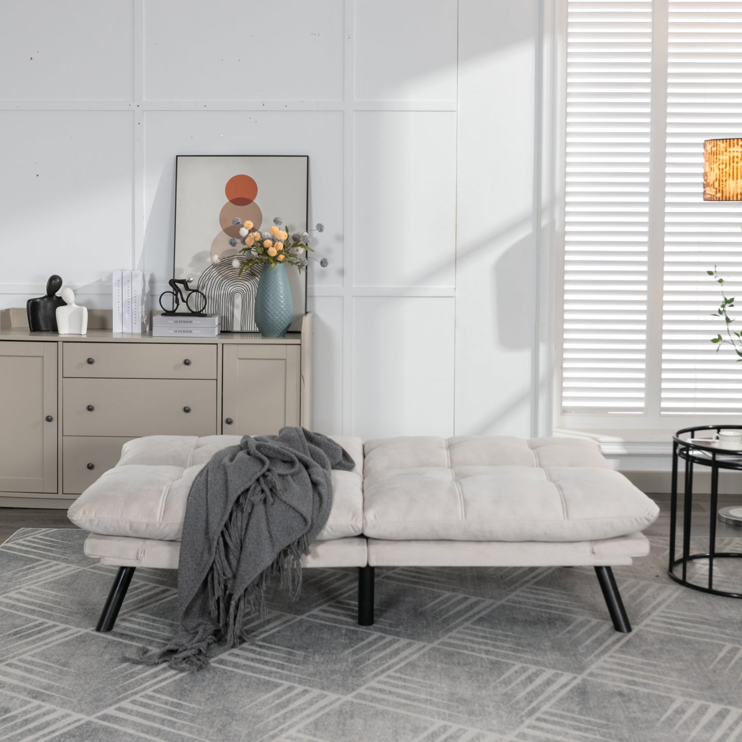 Cream velvet tufted sofa bed with black metal legs and grey throw blanket