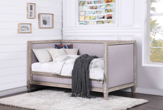 Grey upholstered daybed with whitewashed wood frame and decorative nailhead trim