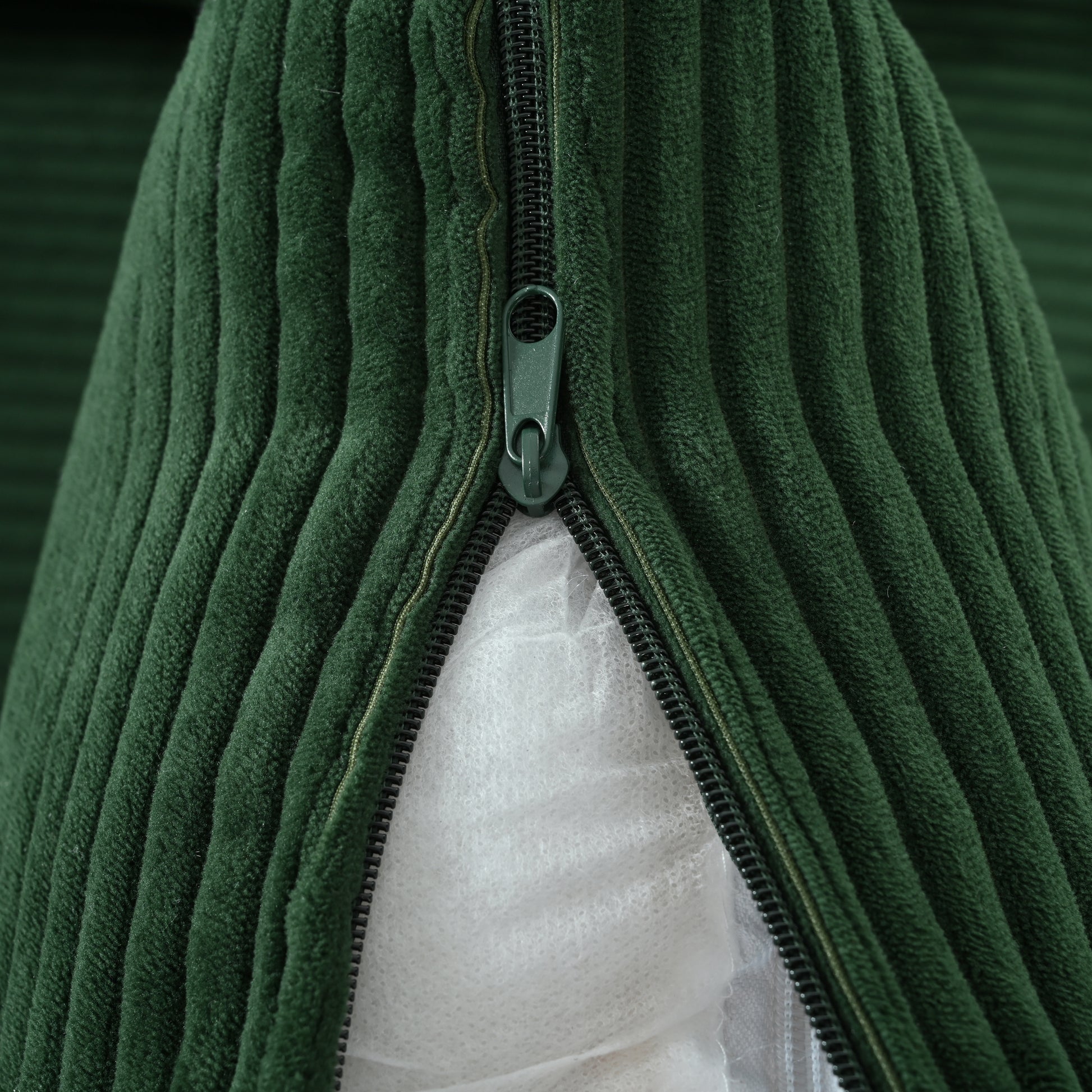 Dark green corduroy fabric with a black zipper partially open revealing white batting