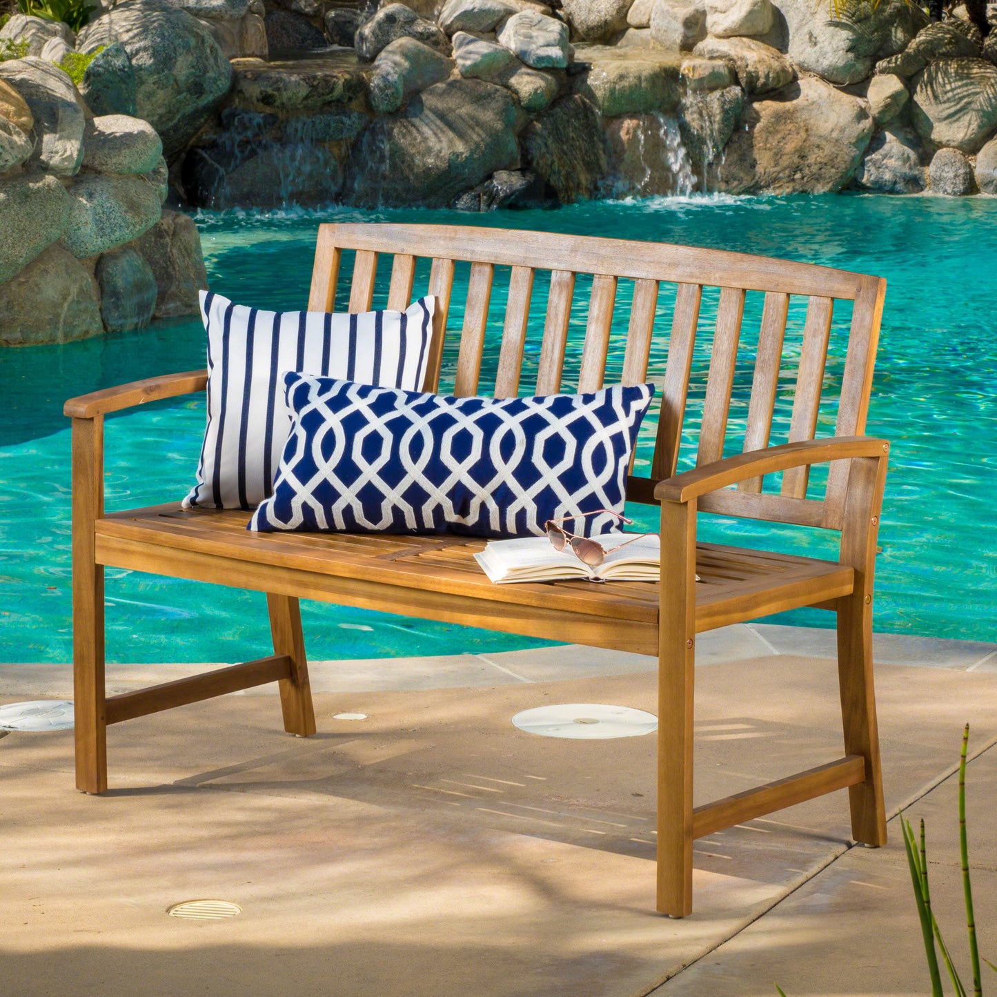 Wooden outdoor bench with blue and white striped and geometric patterned cushions by a pool