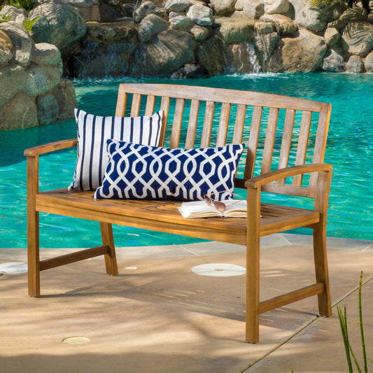 Wooden outdoor bench with blue and white striped and geometric patterned cushions by a pool
