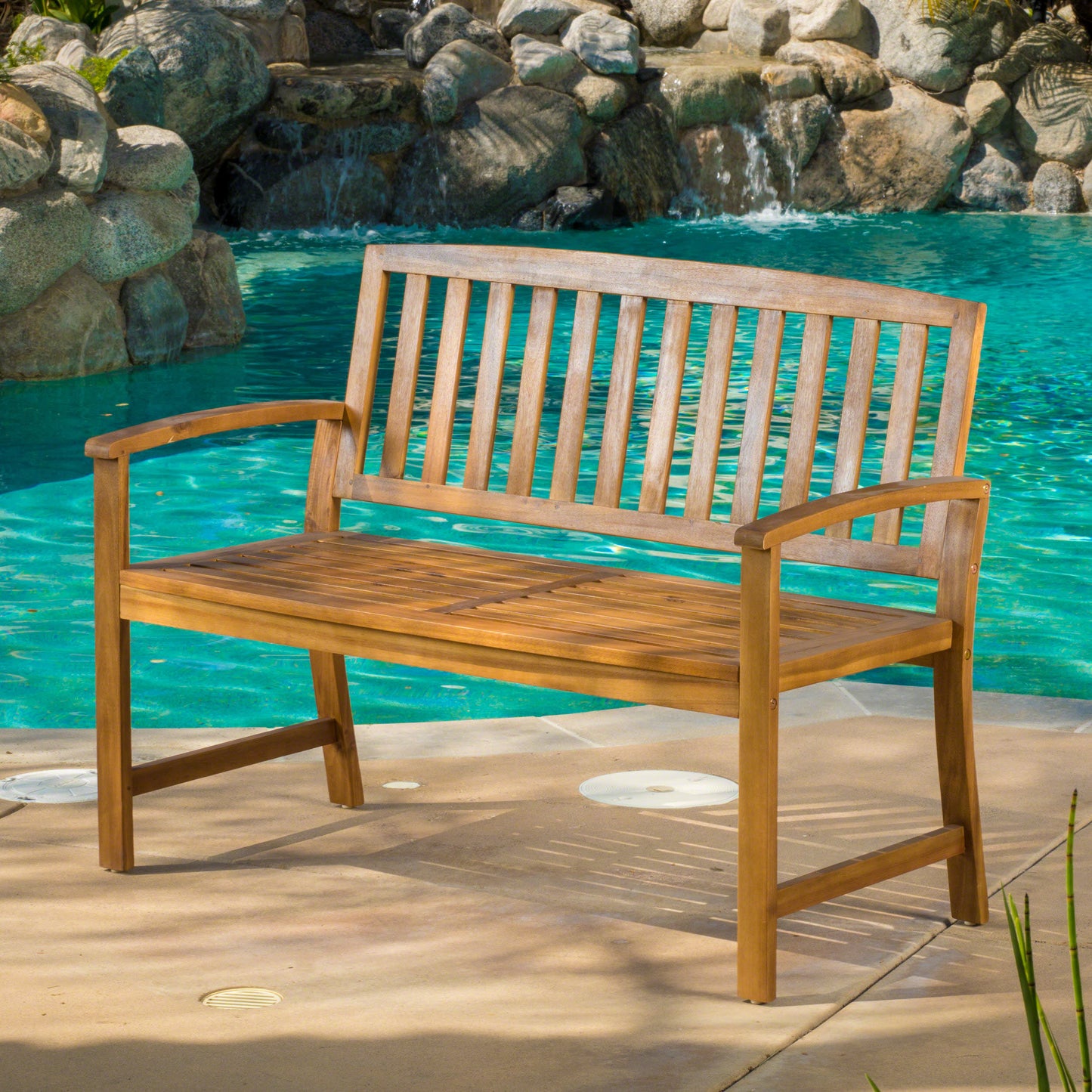 Natural wood patio bench with slatted seat and back placed by a pool