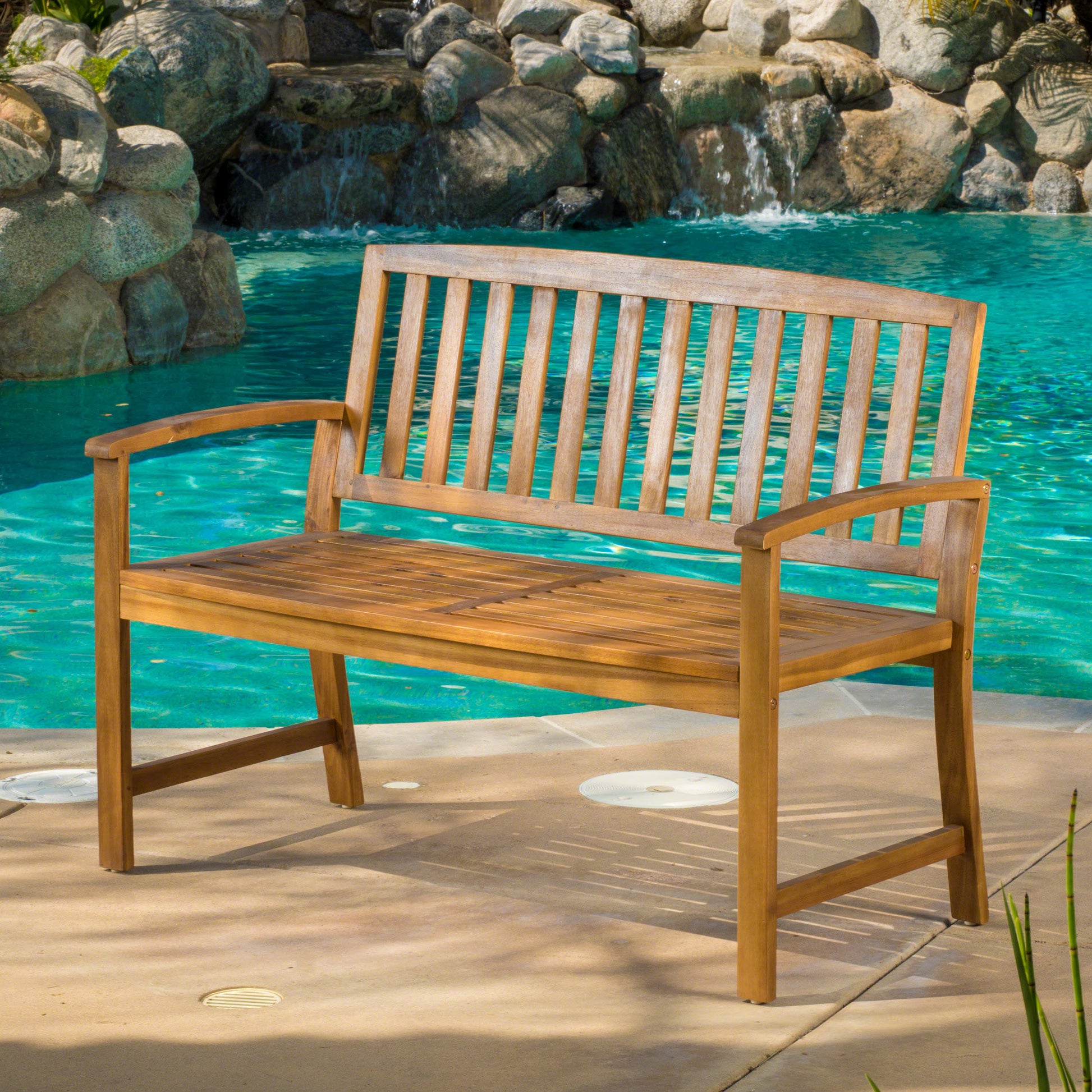 Natural wood patio bench with slatted seat and back placed by a pool