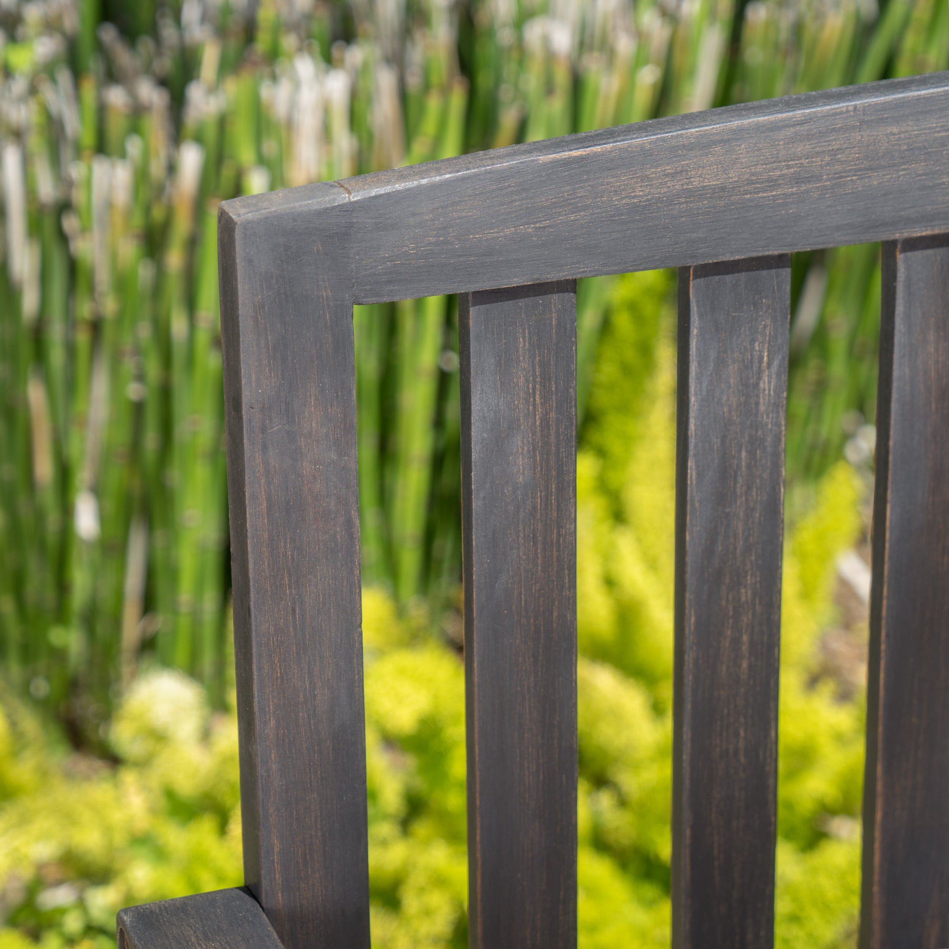 Dark wood outdoor bench slat detail with blurred green foliage background