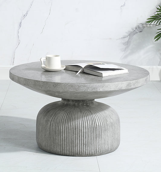 Round grey concrete coffee table with ribbed pedestal base and a book
