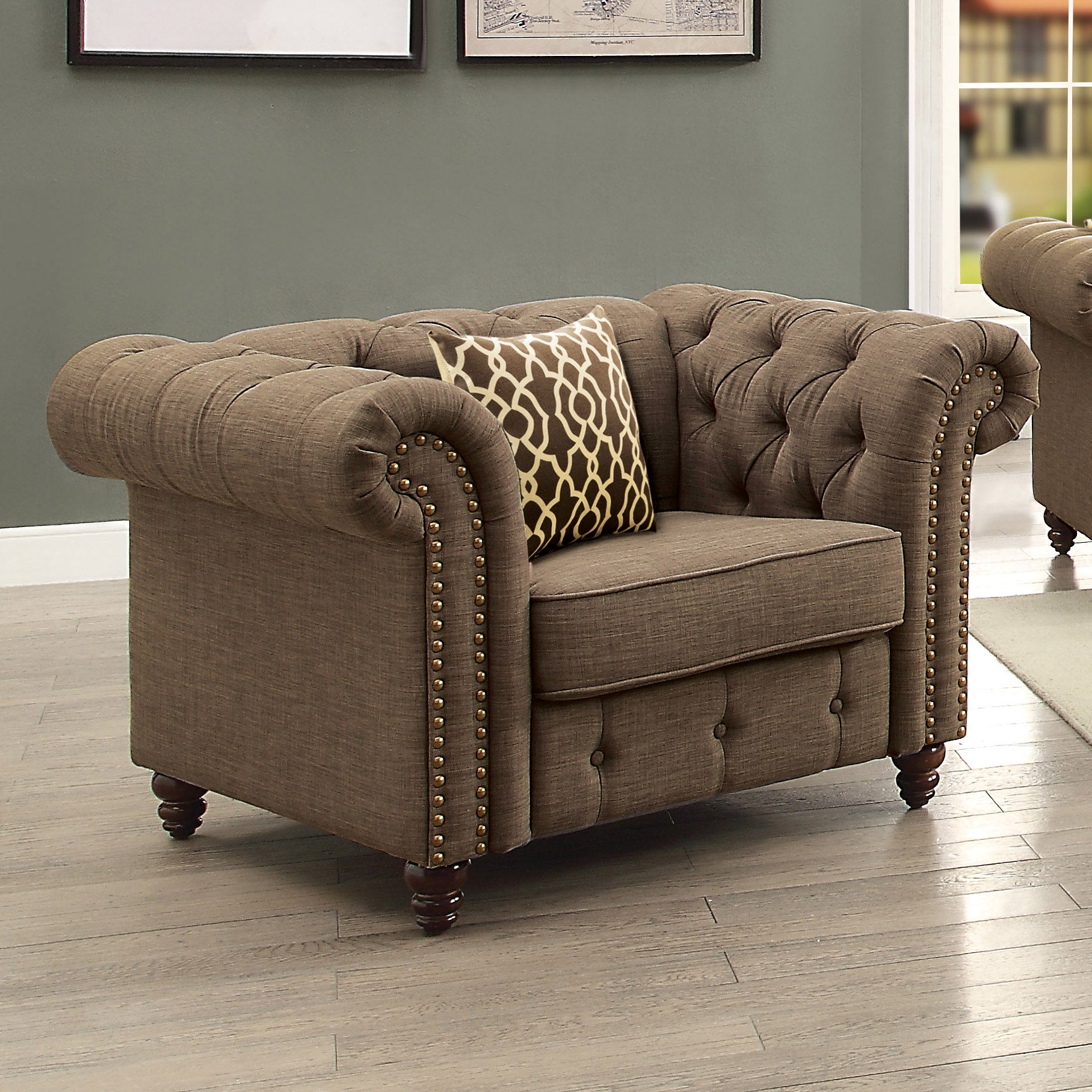Brown fabric chesterfield armchair with button tufting and gold nailhead trim featuring a decorative pillow